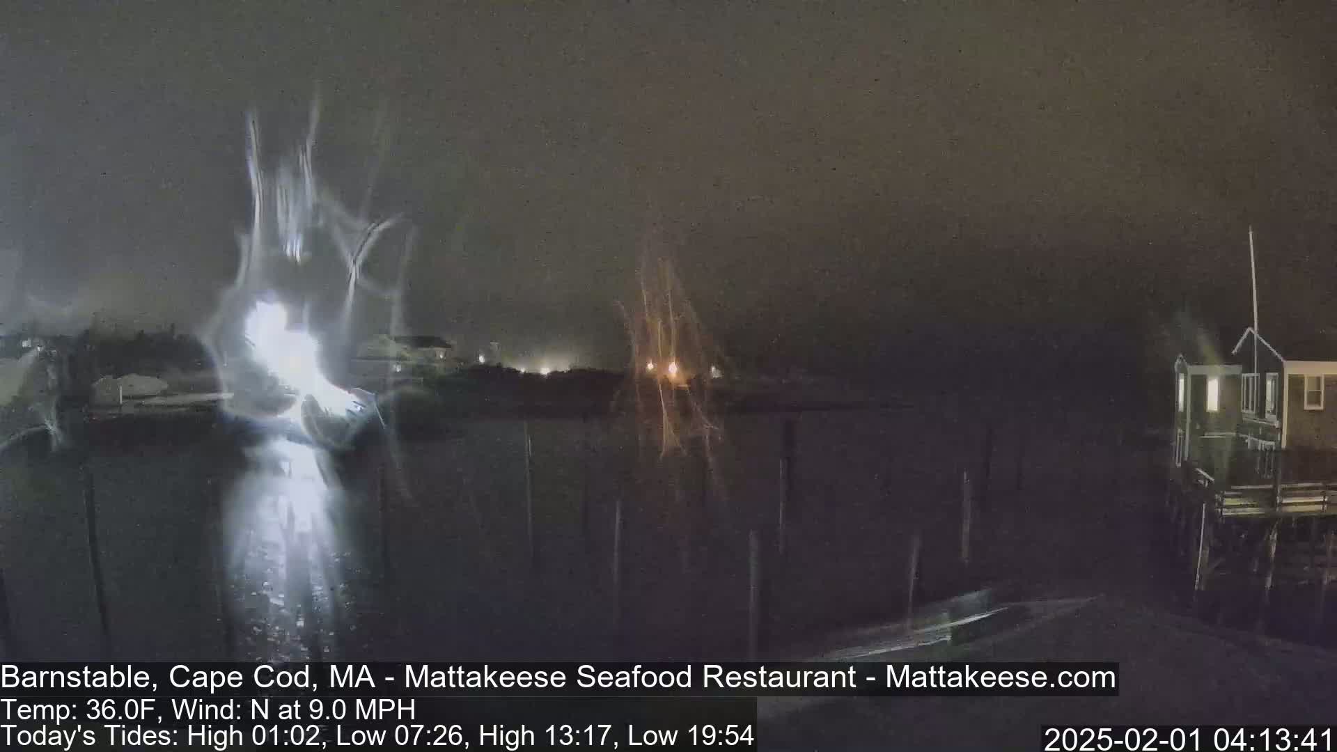 A nighttime, rain-swept waterfront scene shows blurry lights from buildings and what appears to be a pier.