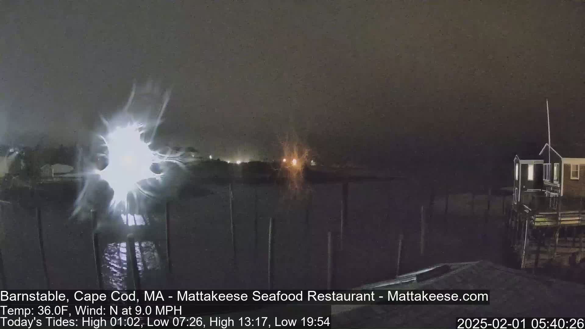 A nighttime view of a waterfront scene with a bright light source in the center, under a dark, possibly snowy sky.