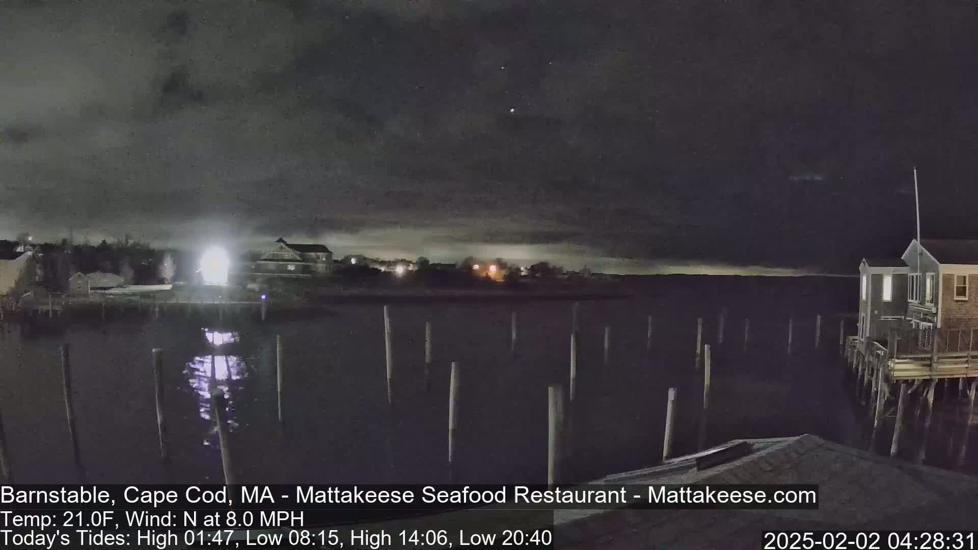 A nighttime view of a calm body of water with pilings, buildings on the shore, and a mostly clear sky.