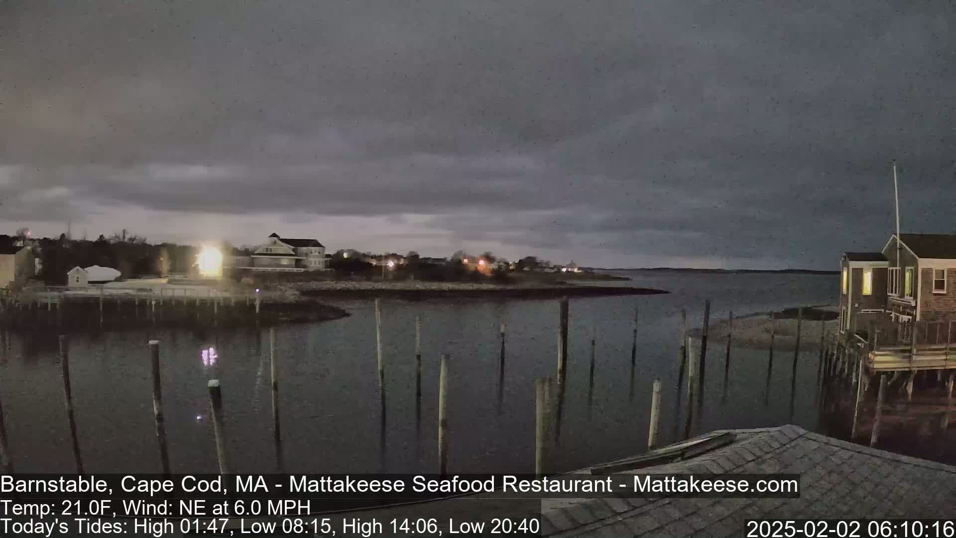 A nighttime view of a calm body of water with a few houses and a dock visible under a cloudy sky.