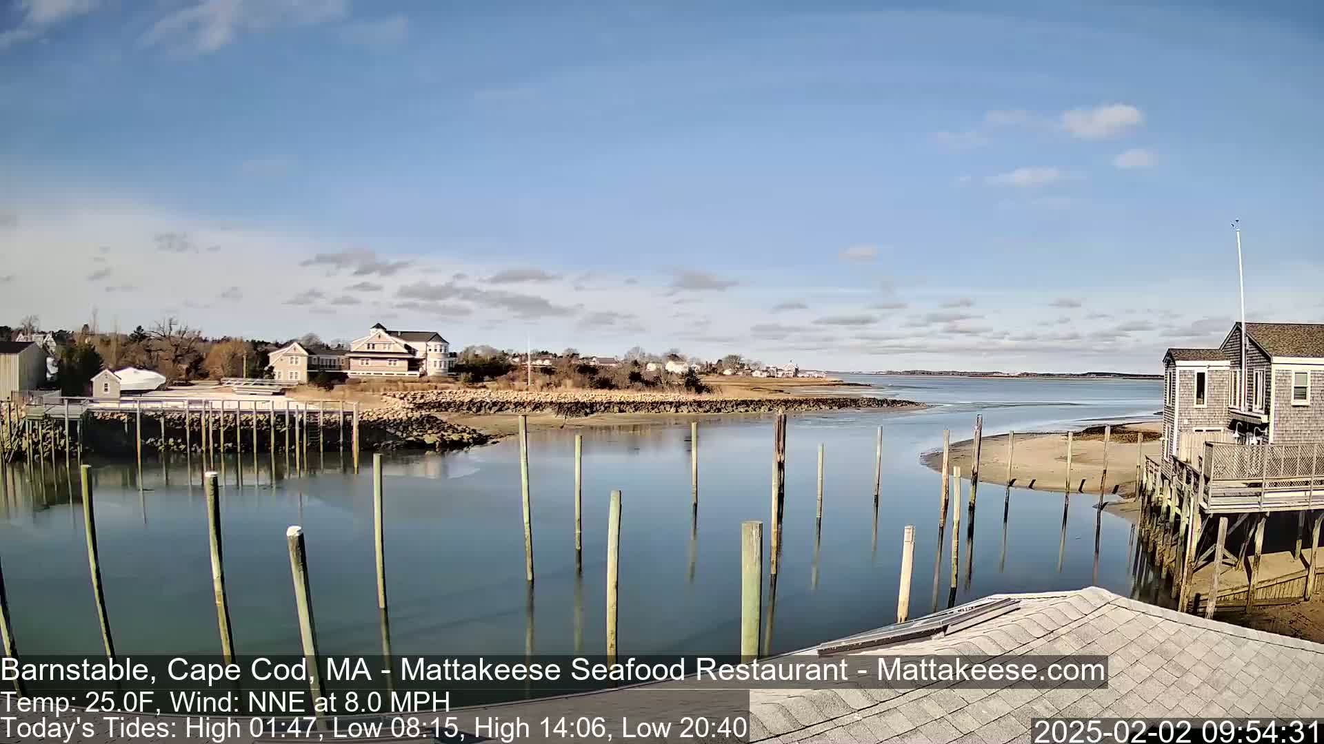 A calm body of water with wooden pilings, houses, and a mostly clear sky.