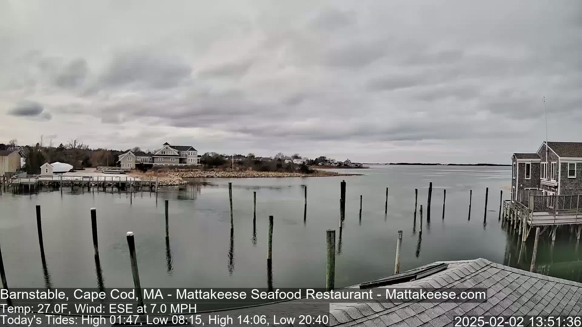 A calm body of water with wooden pilings and buildings along the shore under an overcast sky.