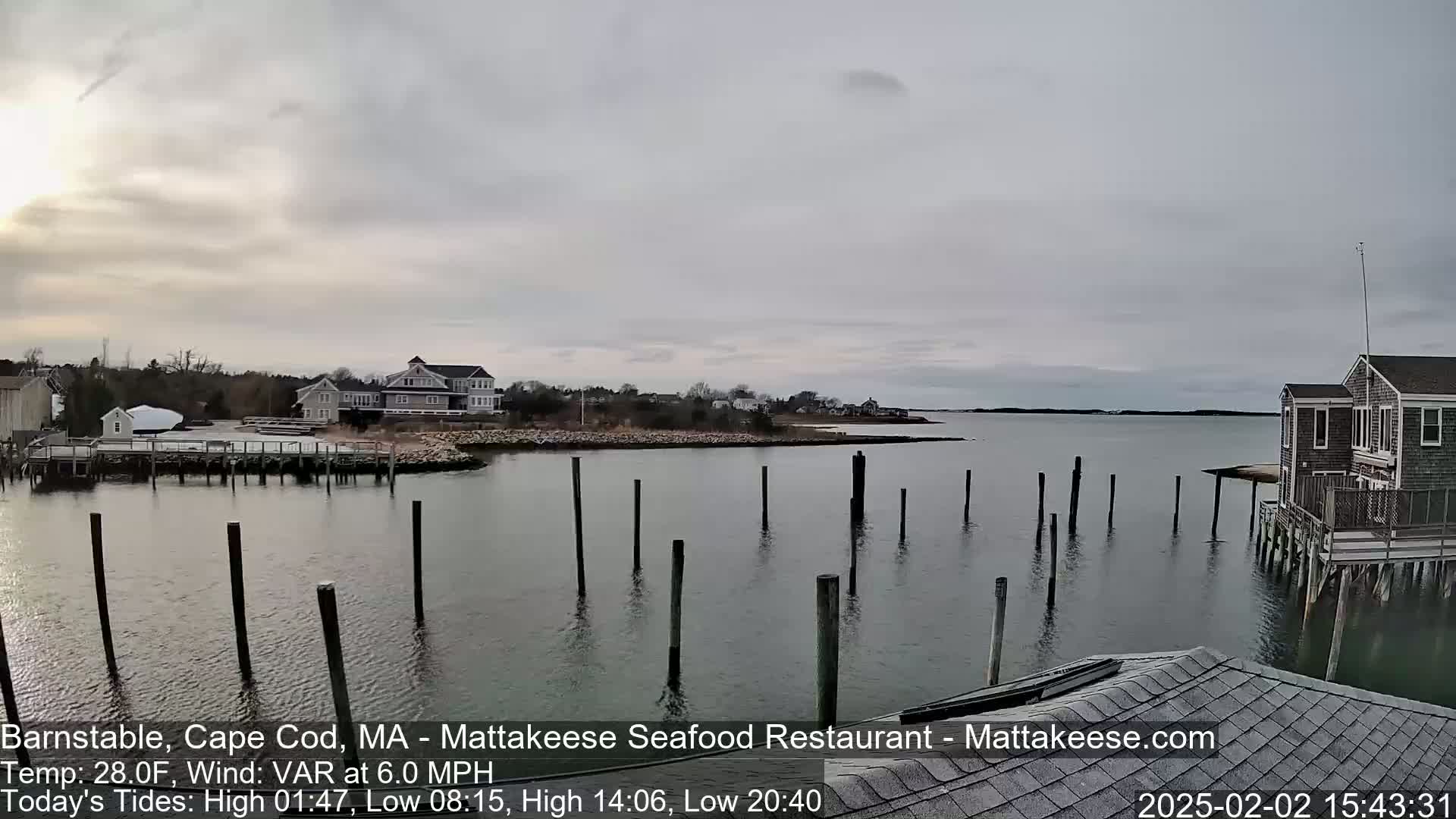 A calm, overcast day reveals a waterfront scene with houses, docks, and pilings in a harbor.