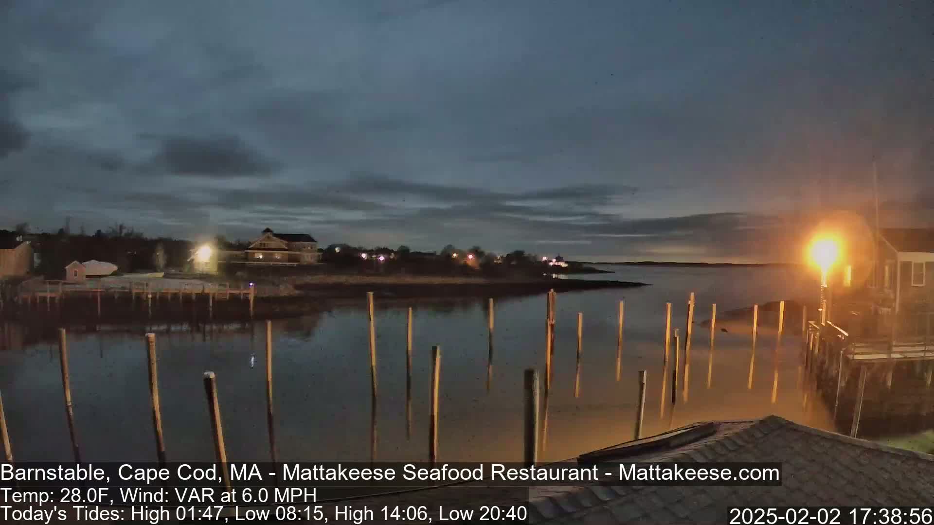 A calm body of water at dusk, reflecting lights from buildings on the shore, with numerous posts extending from the water's edge.