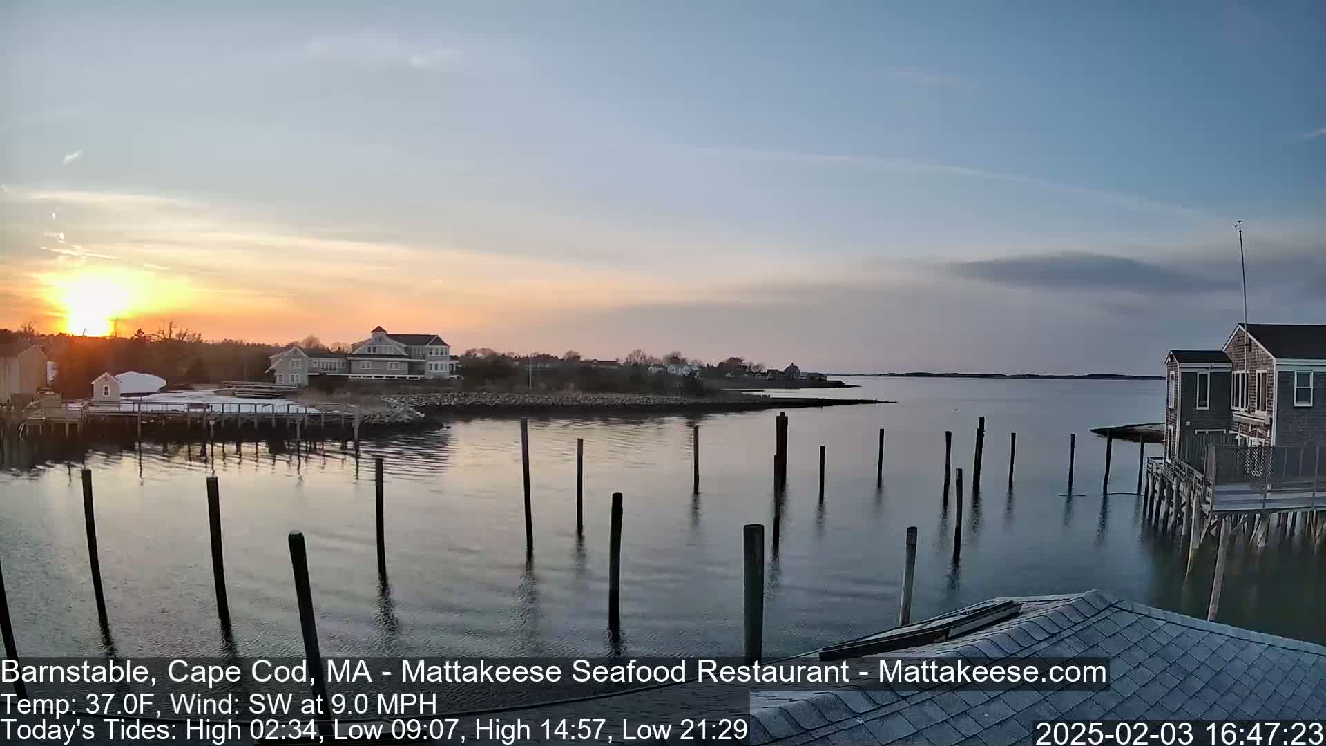 A calm sunset over a harbor with several houses and a dock, under a mostly clear sky.
