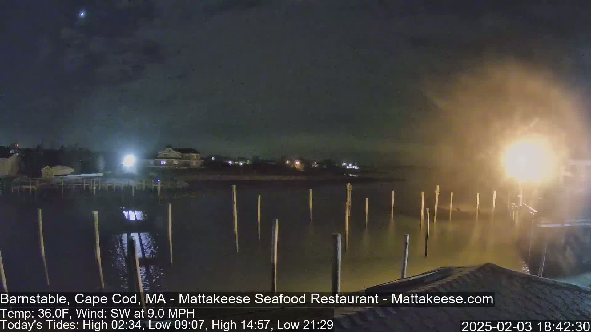 A nighttime view of a calm body of water with wooden posts extending from the shore under a hazy sky with a southwest wind.