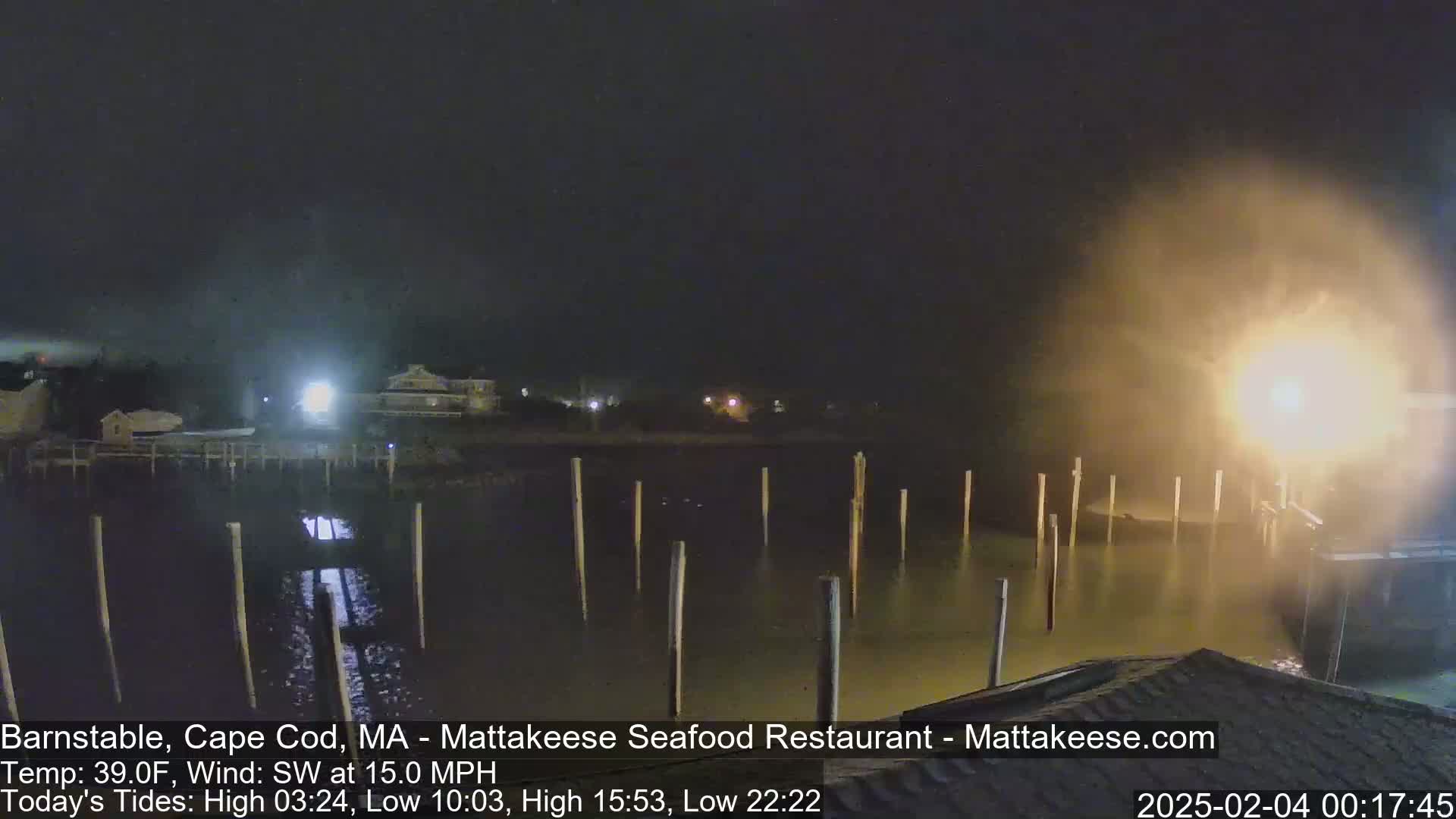 A nighttime view of a calm body of water with pilings, illuminated by lights from nearby buildings, under foggy conditions with a southwest wind.