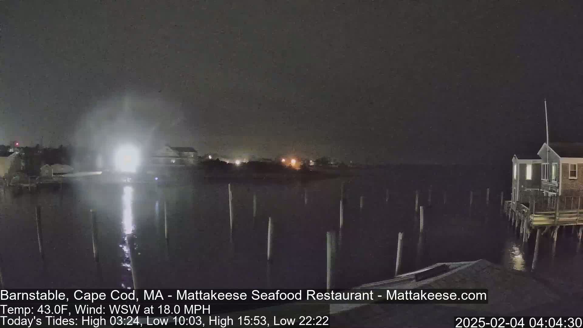 A nighttime view of a calm body of water with pilings and buildings along the shore under a dark, cloudy sky.