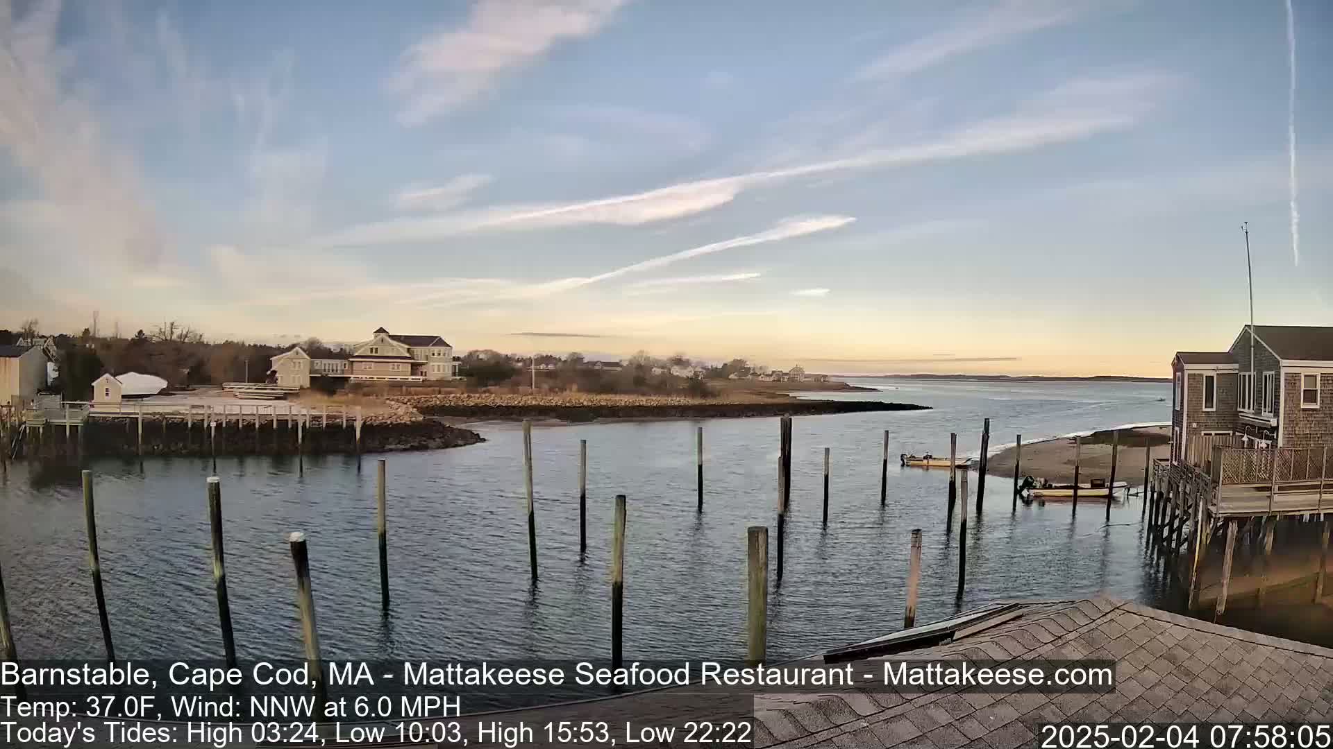 A calm body of water with several boats and wooden pilings, under a partly cloudy sky.