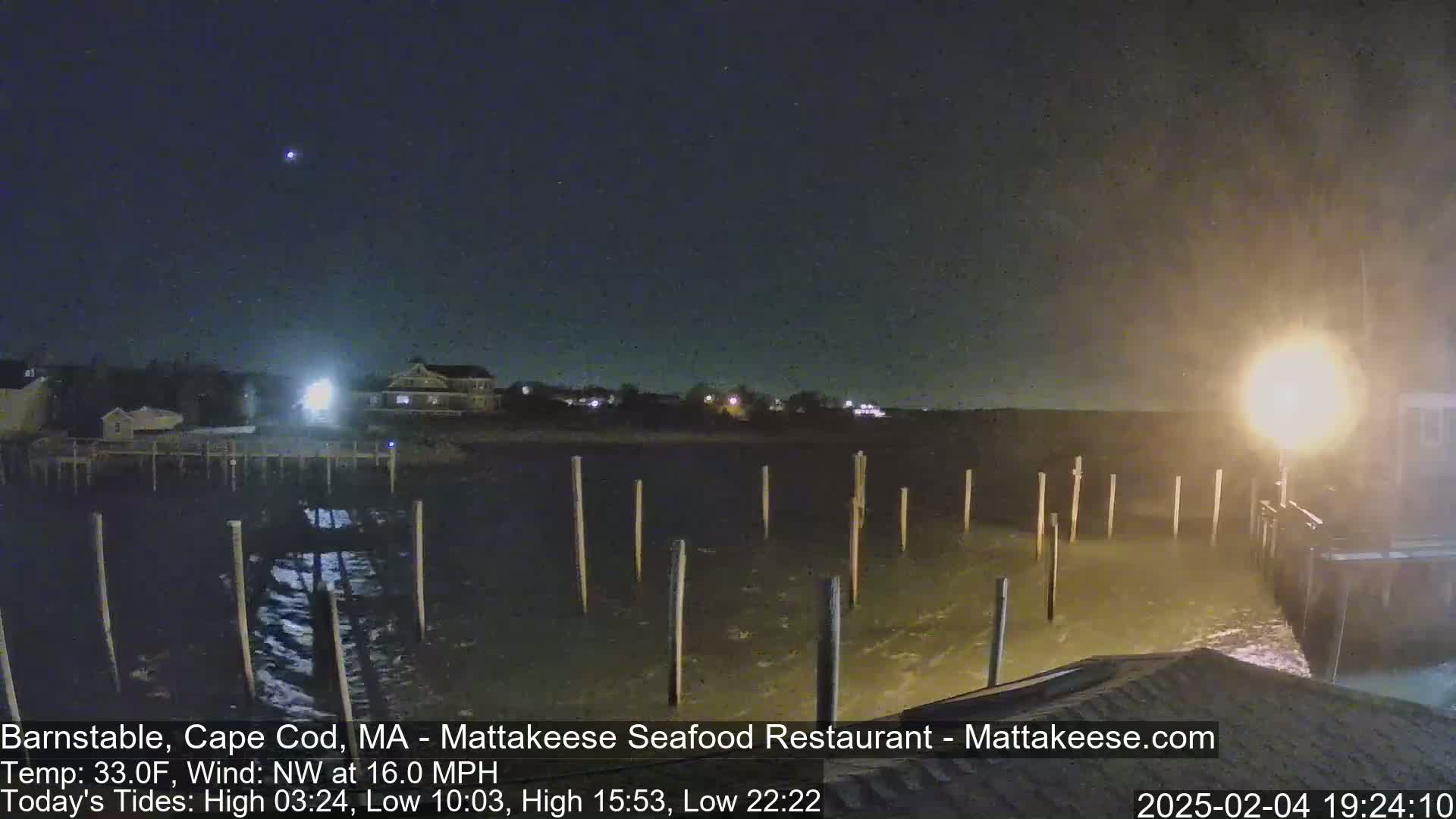 A nighttime view of a partly cloudy waterfront scene with choppy water under a pier, illuminated by a bright light.
