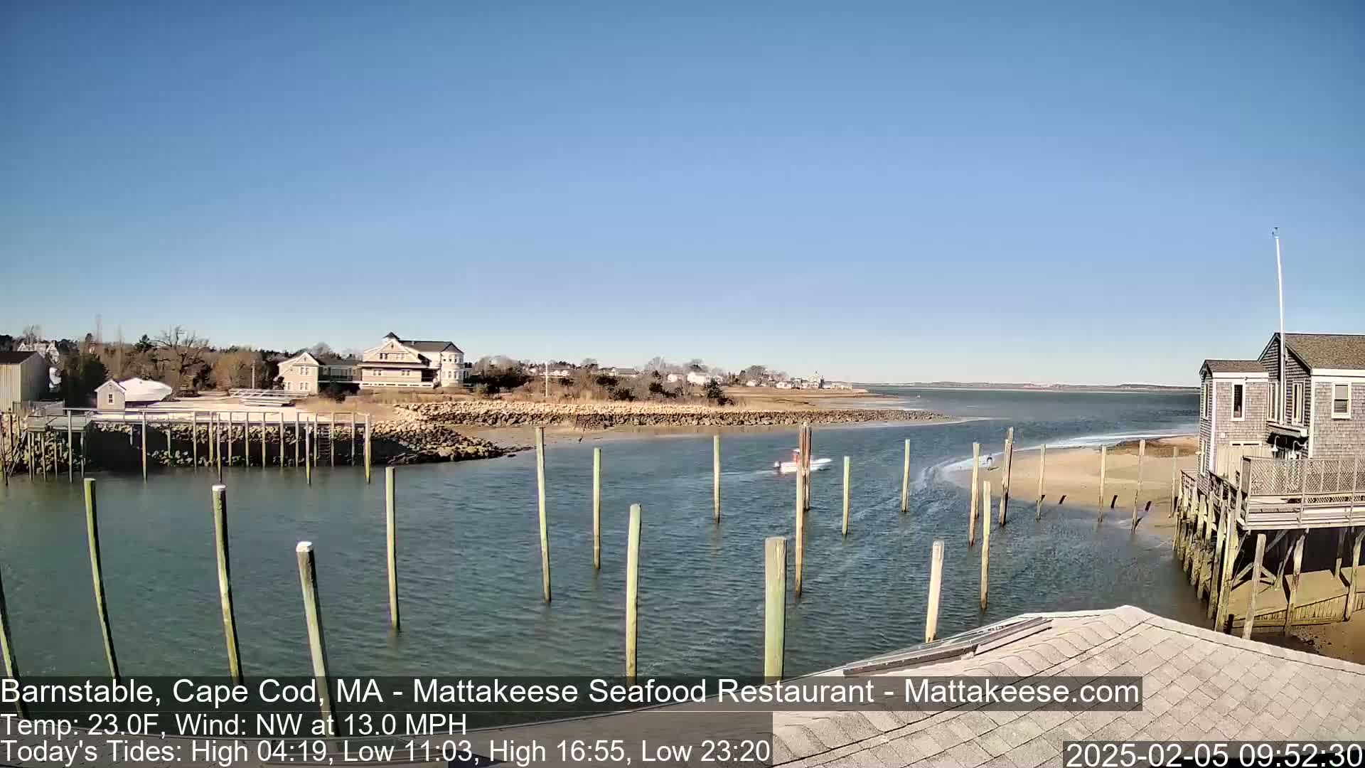 A calm, sunny day shows a small boat traveling through a narrow waterway near a waterfront residential area with a building on pilings.