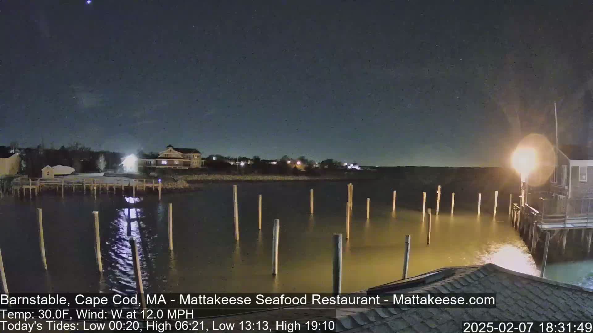 A nighttime view of a calm body of water with docks and buildings under a clear, starry sky.