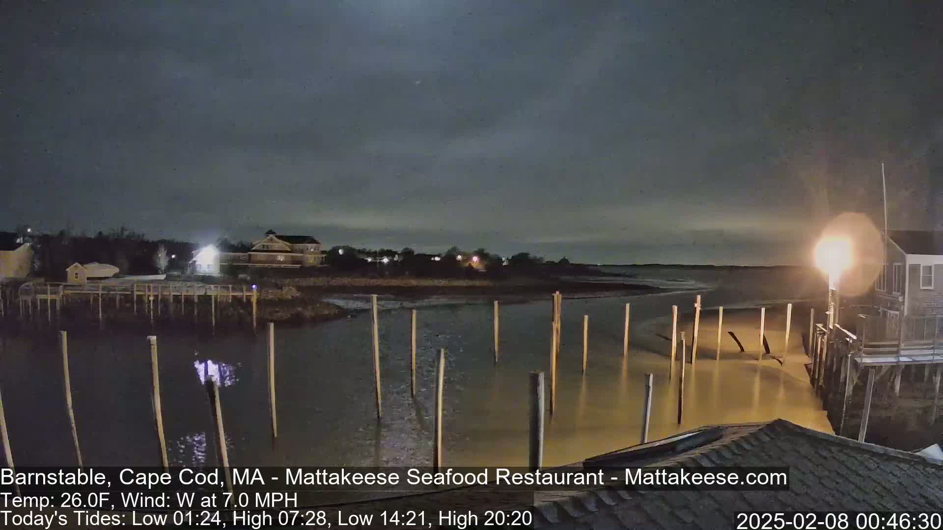 A nighttime view of a calm waterway with wooden pilings, illuminated buildings, and a dark sky.