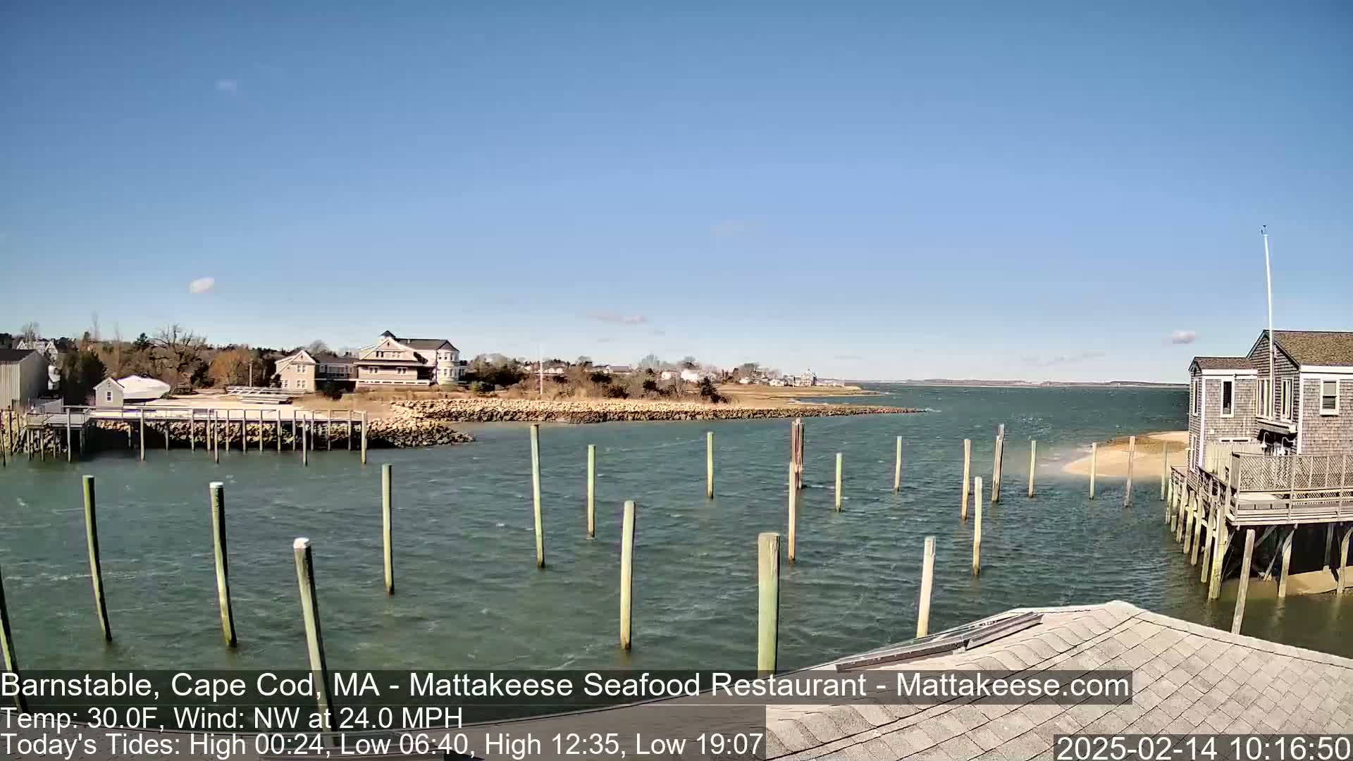 A waterfront scene on a sunny day with a northwest wind shows a calm body of water with wooden pilings and several buildings along the shore.