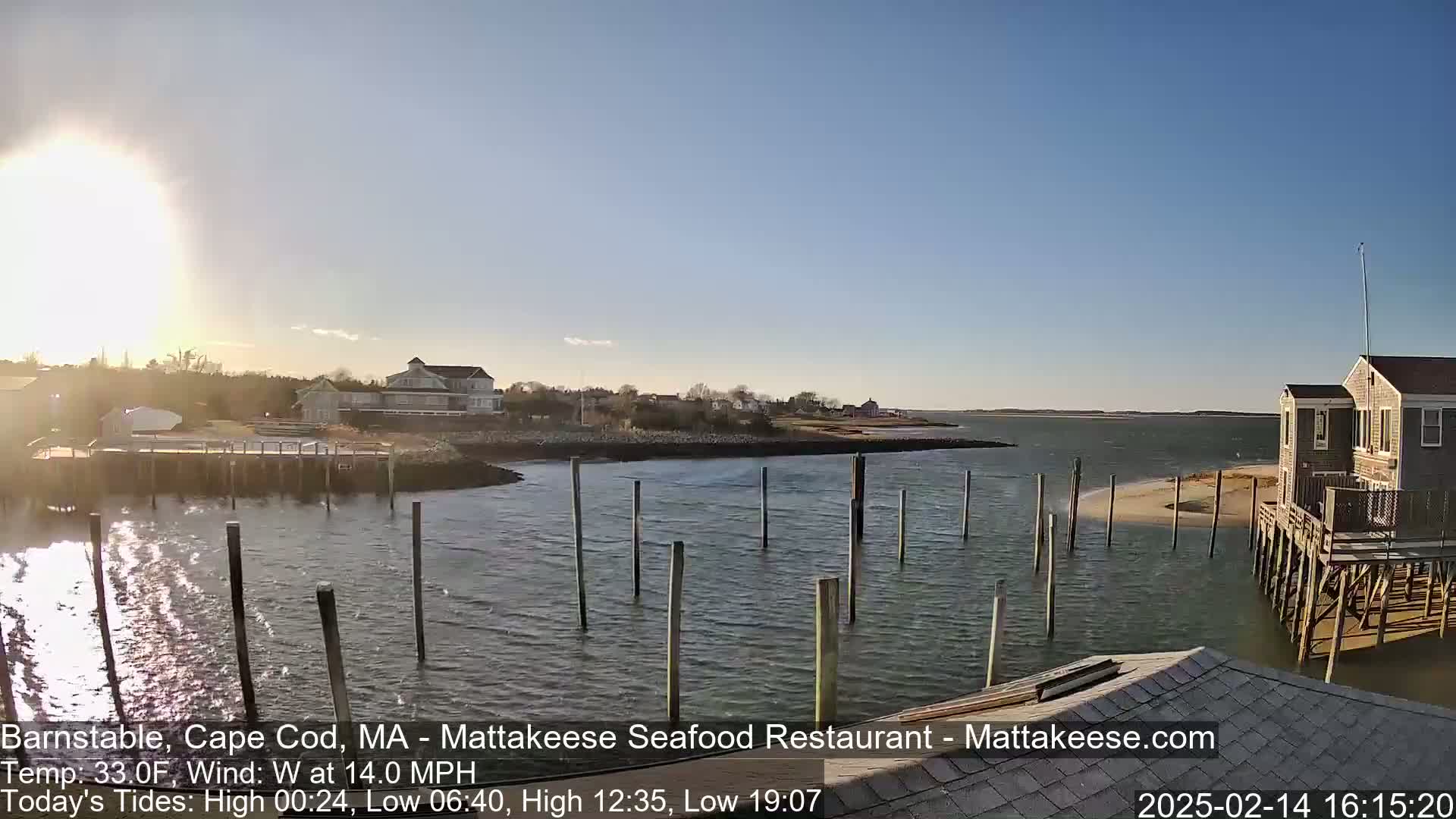 A sunny day on a calm body of water shows a waterfront scene with houses, docks, and pilings, and a sandy shoreline.
