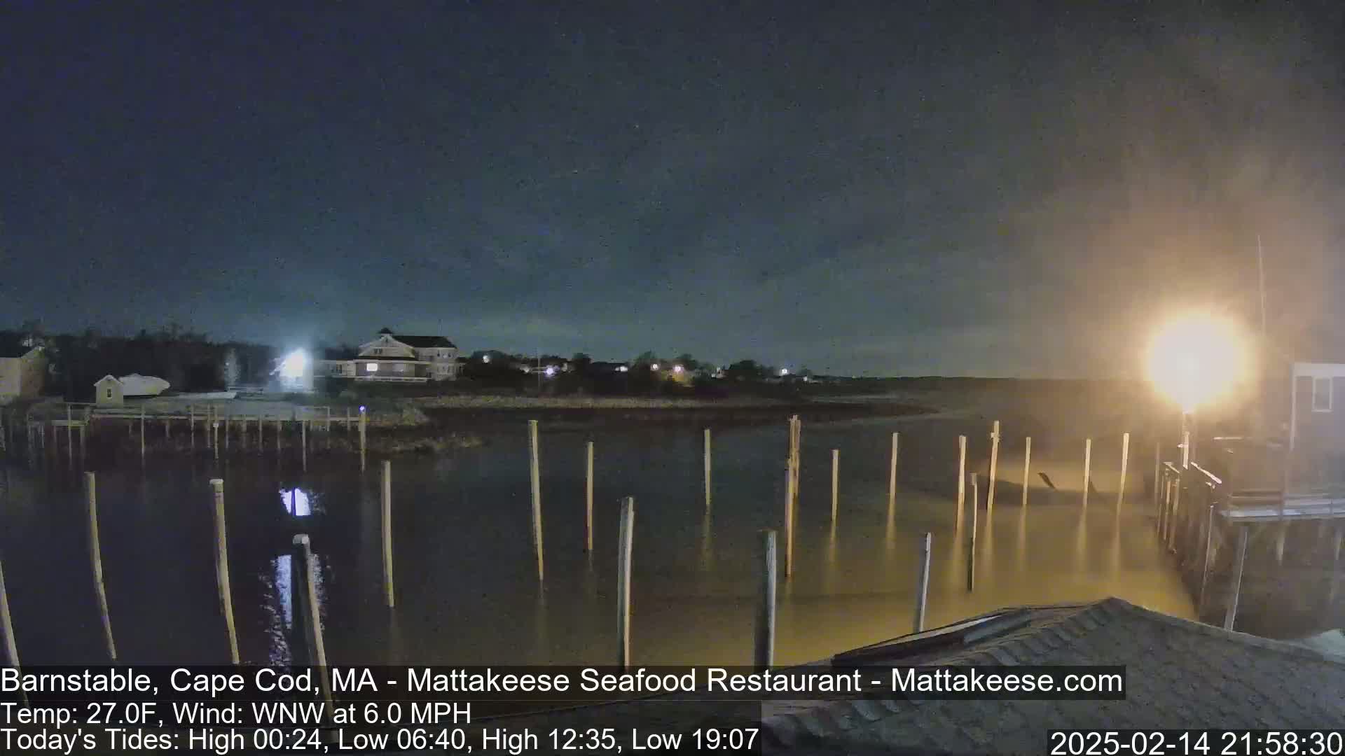 A nighttime view of a calm body of water with pilings and a building in the background under a dark, clear sky.