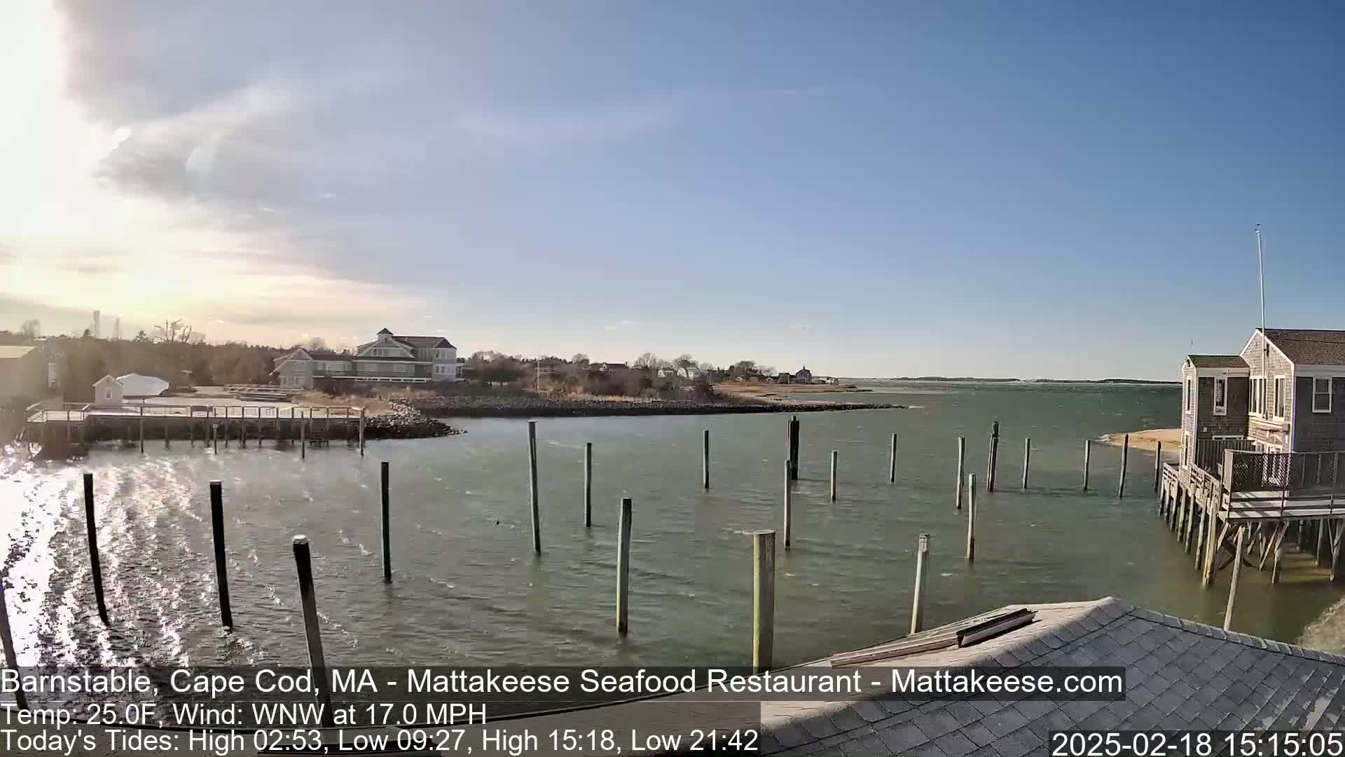 A calm bay with a few houses and a dock in the background under a clear blue sky.