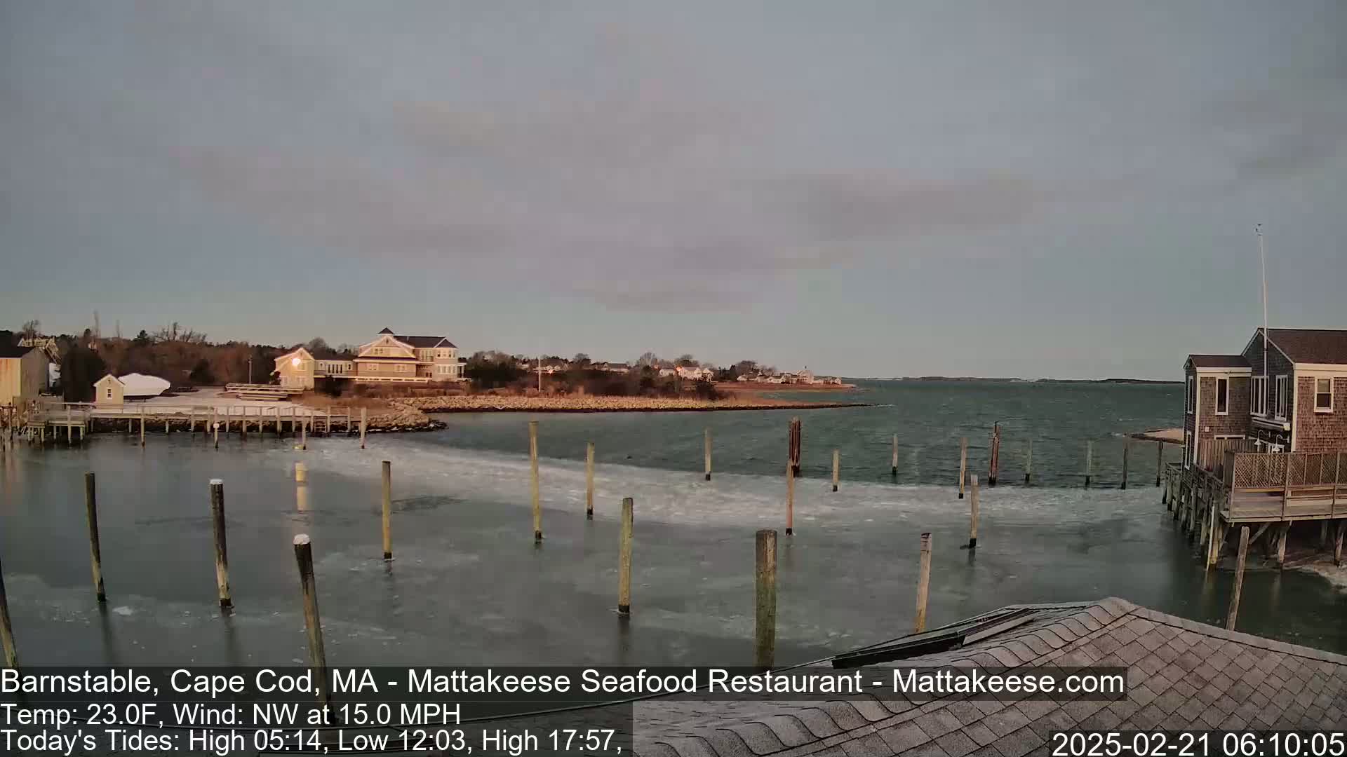 A calm body of water with partial ice coverage near a shoreline with houses and docks under a clear, dusky sky.