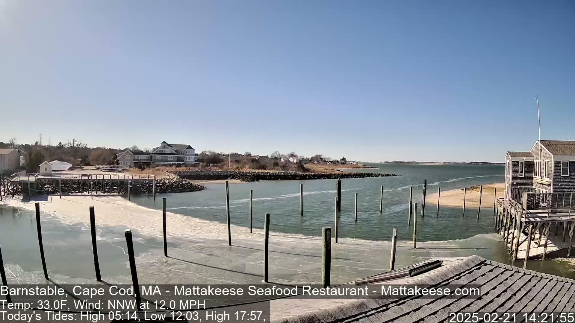 A partially frozen waterway with a small sandbar, docks, and houses visible on a sunny day with a NNW wind blowing at 12.0 mph.