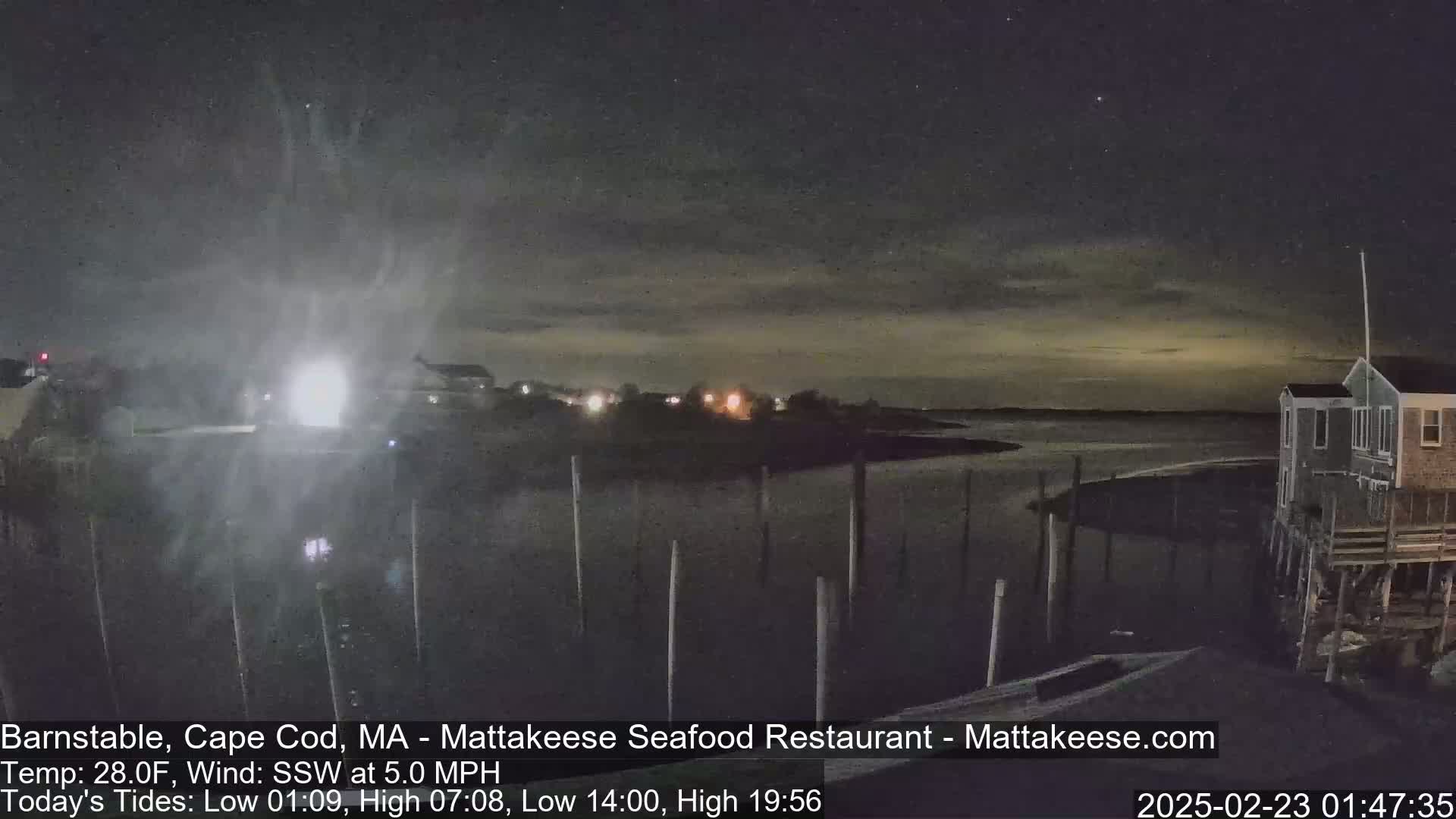 A nighttime view of a calm body of water with a few houses on stilts visible under a mostly clear, dark sky.