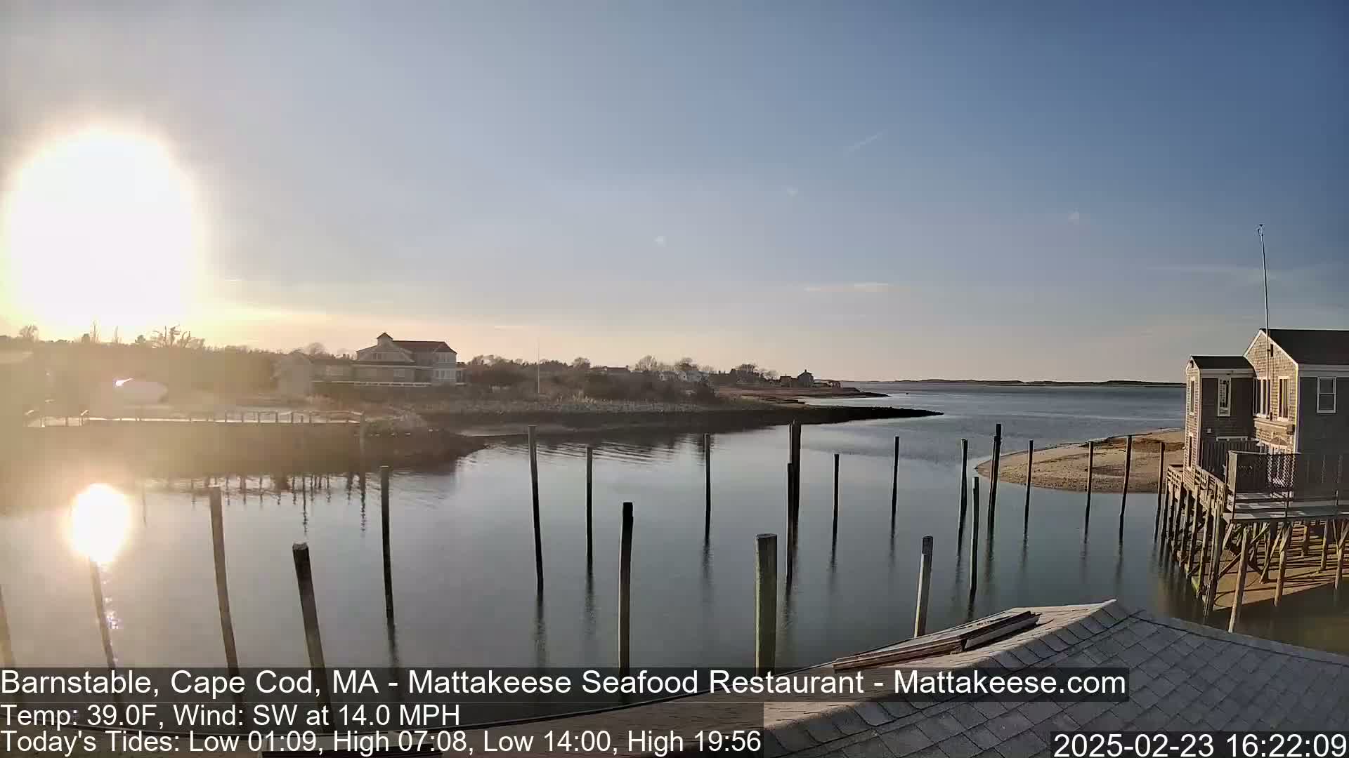 A calm body of water with a dock and buildings on the shore is seen under a bright, sunny sky.