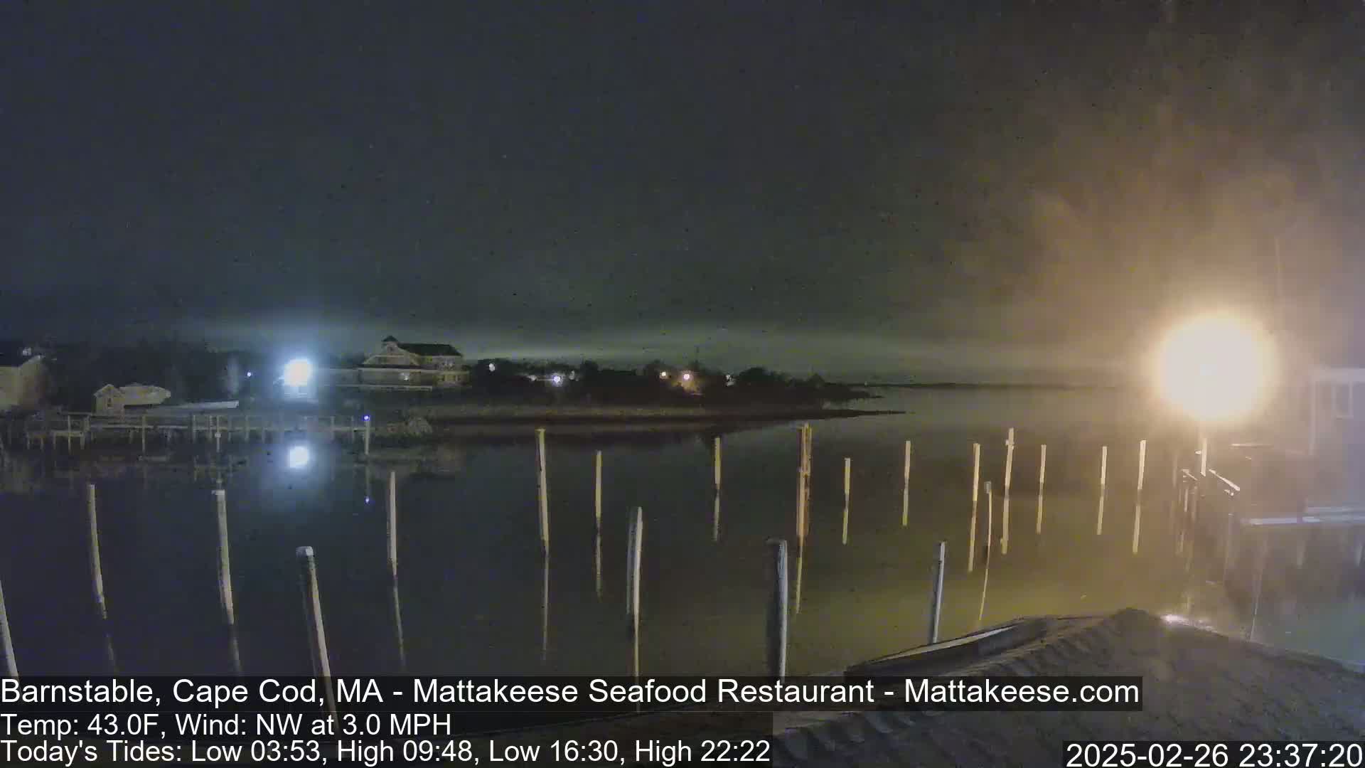 A nighttime view of a calm body of water with pilings extending from a dock into the water under a hazy sky.