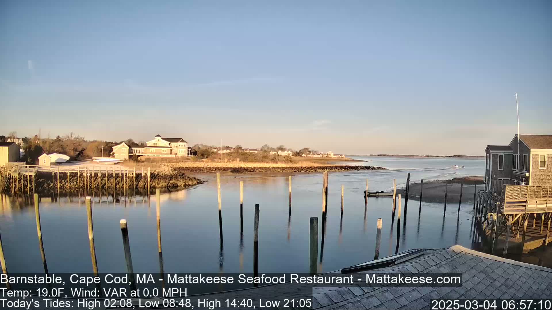 A calm, clear day reveals a waterfront scene with houses, a dock, and calm water reflecting the sky.
