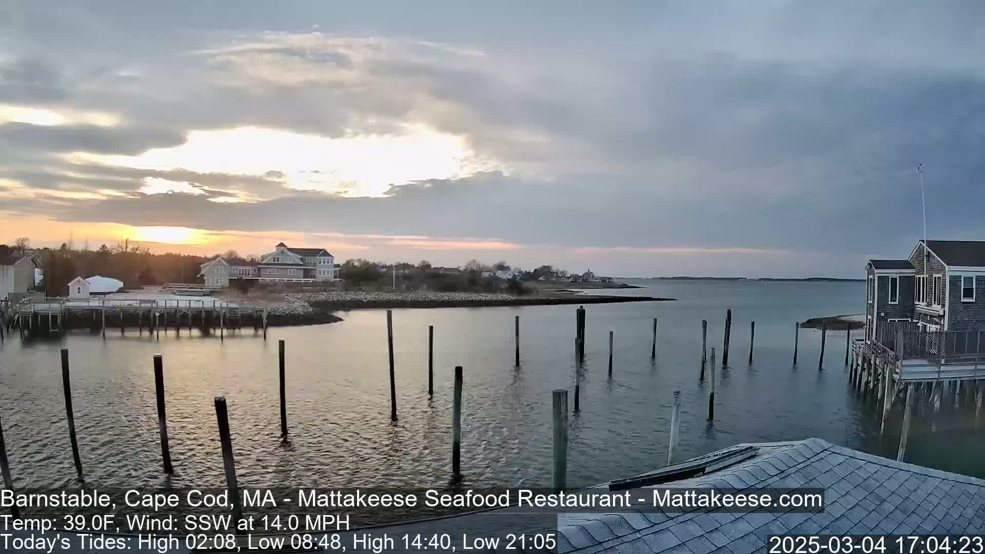 A partly cloudy sunset over a calm harbor with several houses and a dock in the foreground.