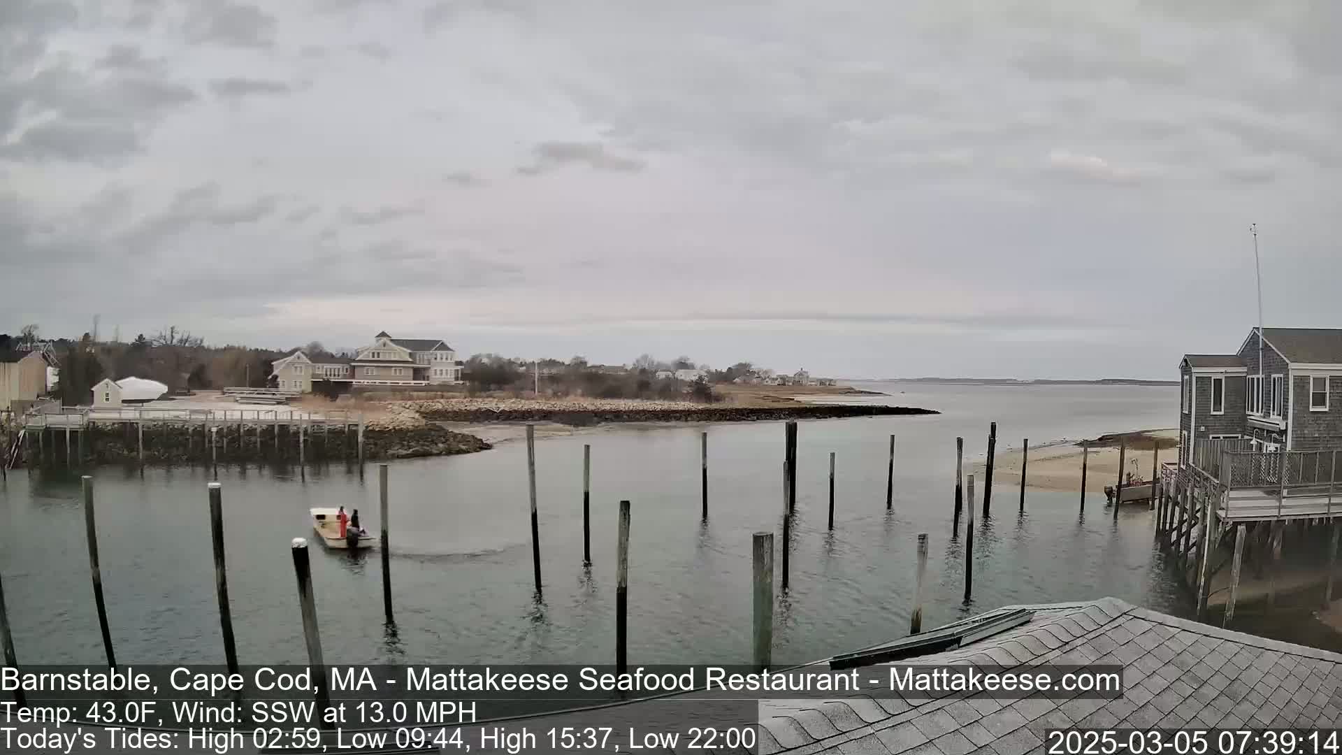 A calm, overcast day shows a harbor with a small boat and several buildings along the shoreline.