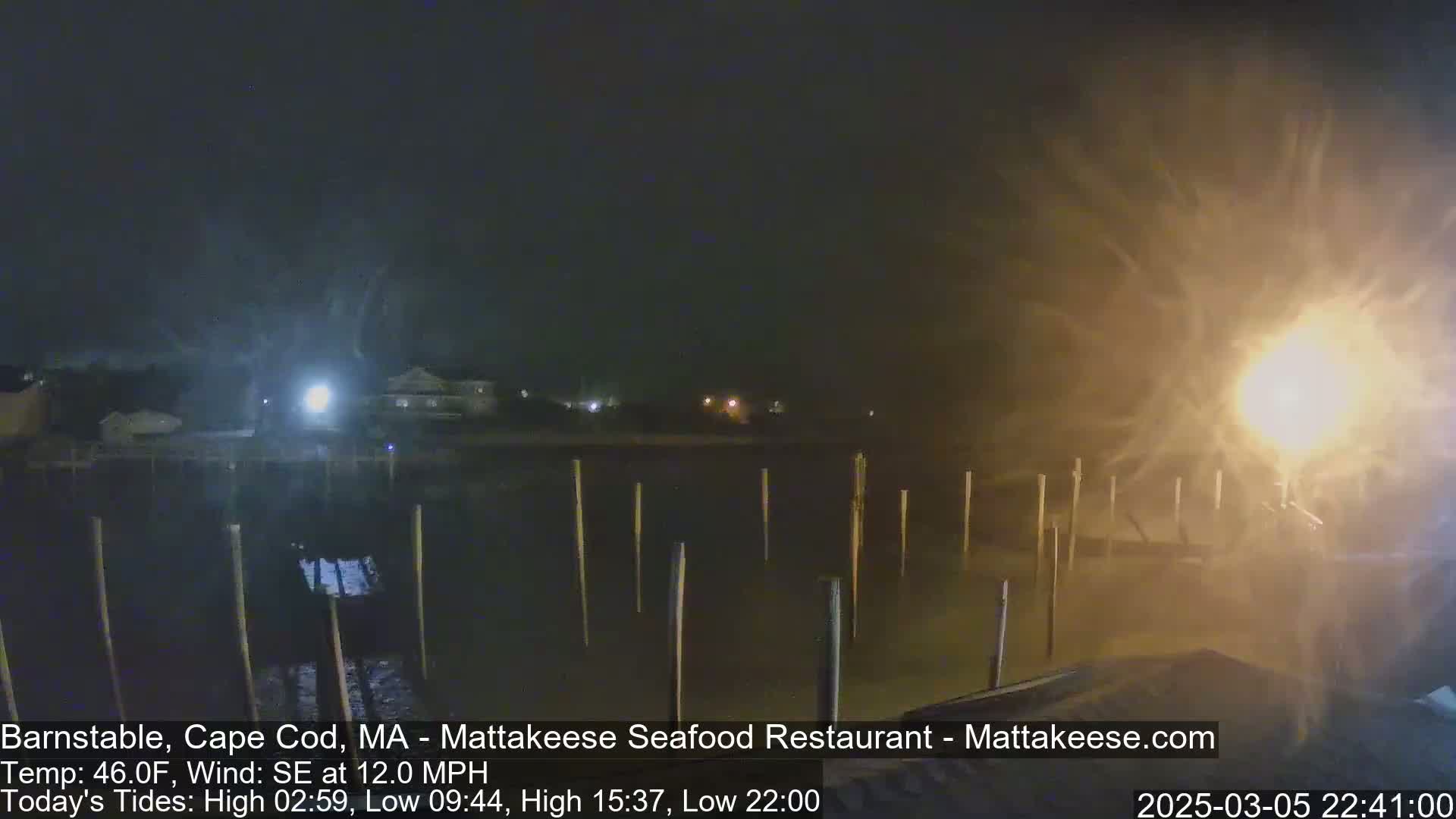 A nighttime view of a harbor with posts in the water, under windy conditions with blowing spray.