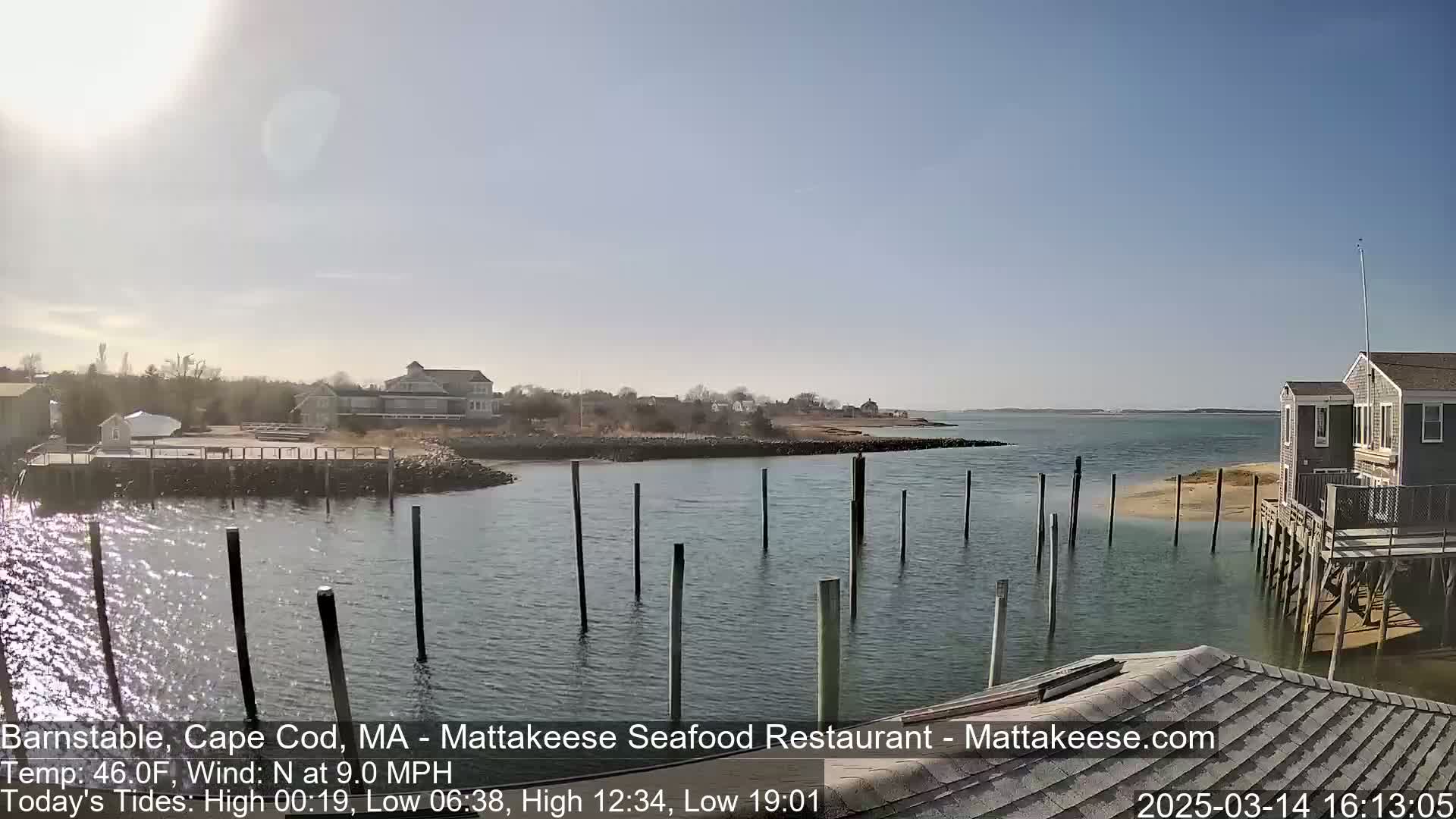 A sunny day reveals a calm body of water with wooden pilings, a small waterfront community, and a few houses on stilts.
