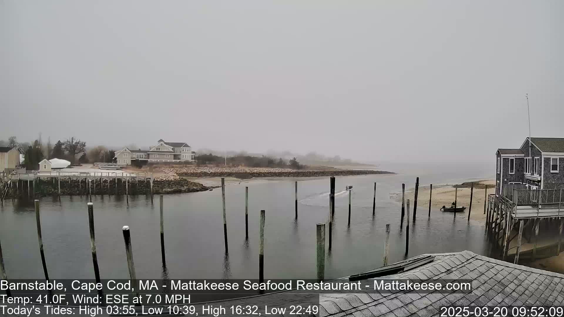 A foggy harbor scene shows a small boat near wooden pilings, with houses and a shoreline visible in the distance.