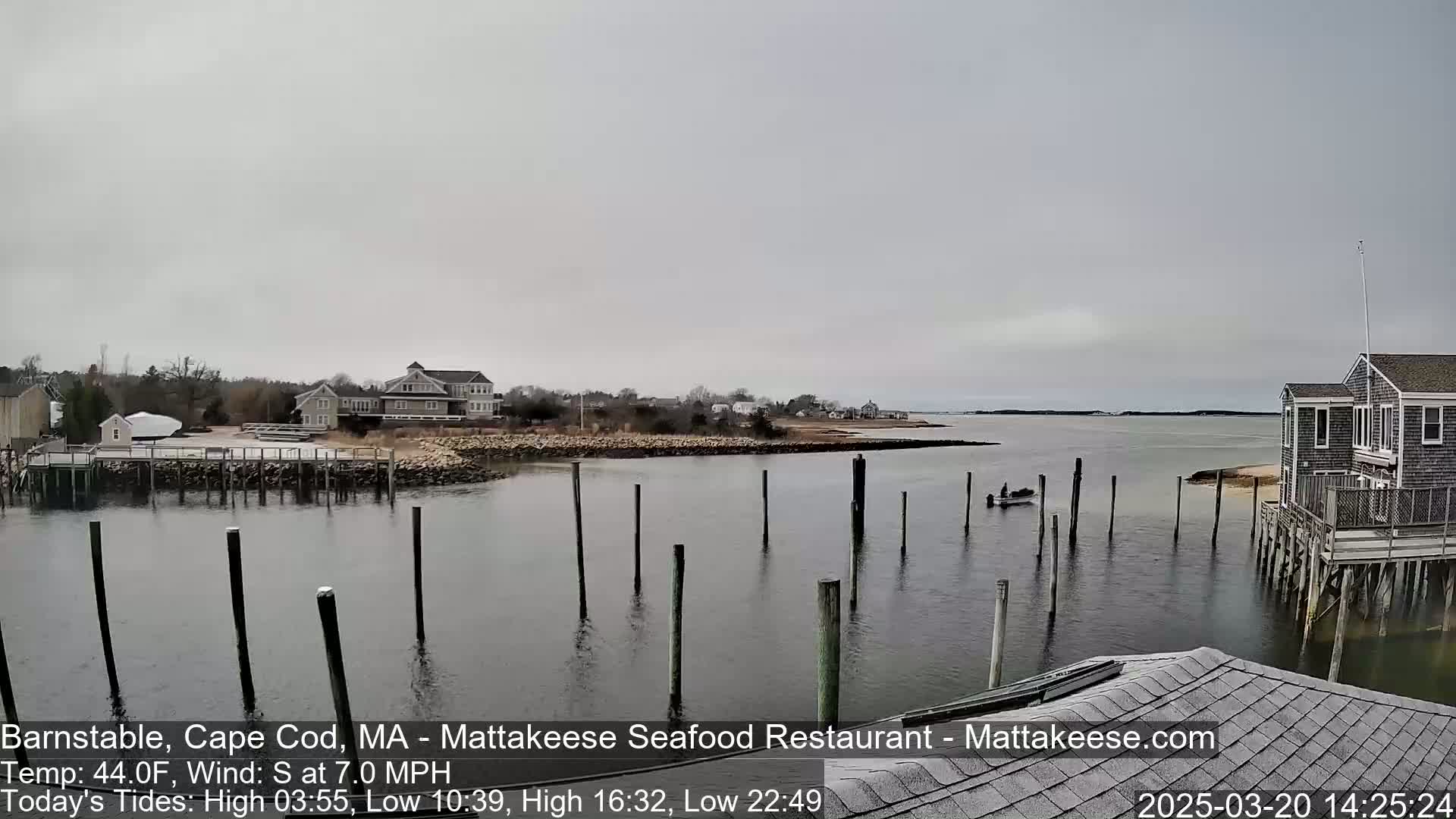 A calm, overcast day reveals a waterfront scene with houses, docks, and a small boat on the water.