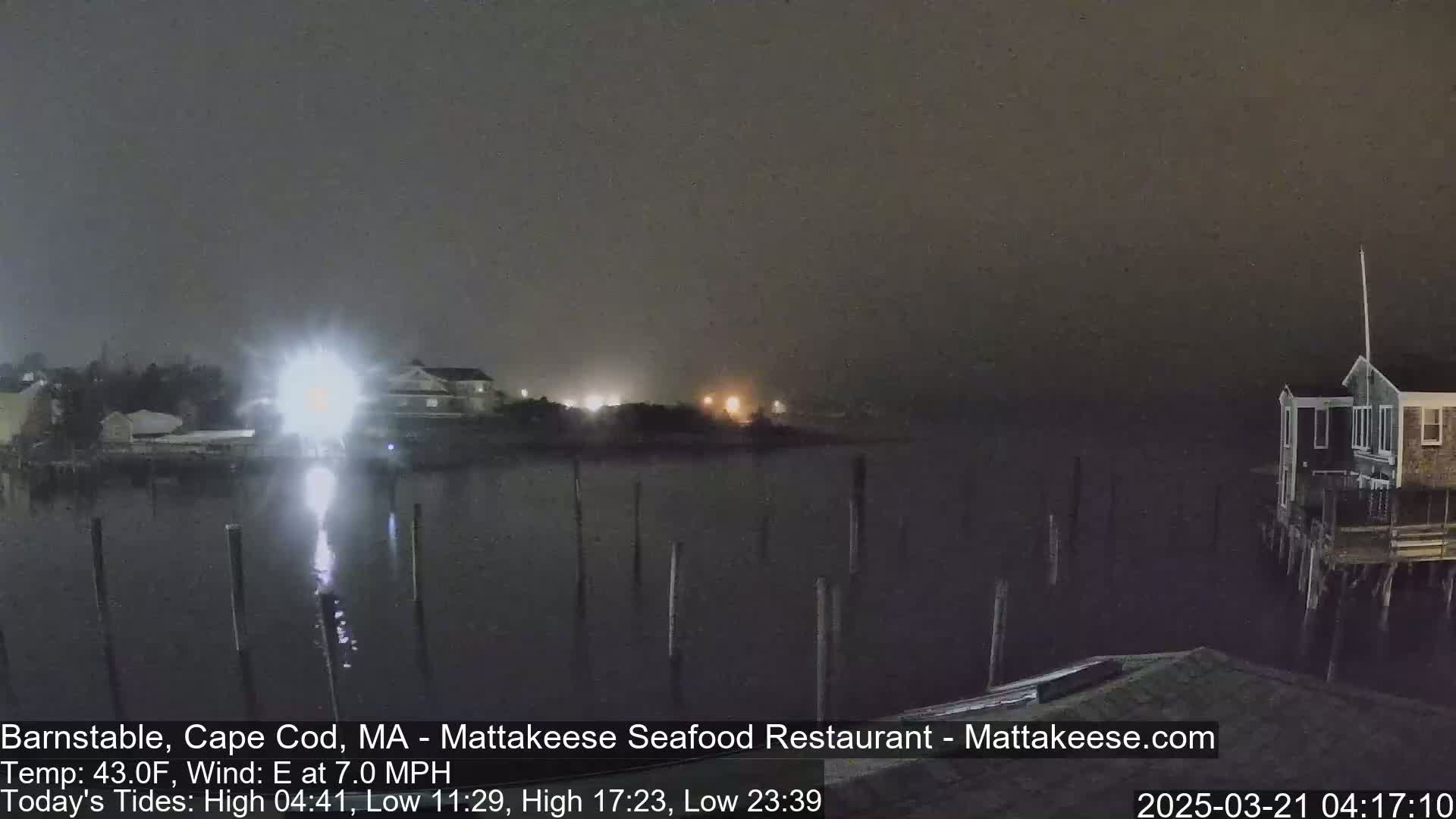 A nighttime view of a calm body of water with buildings and pilings visible in hazy conditions.