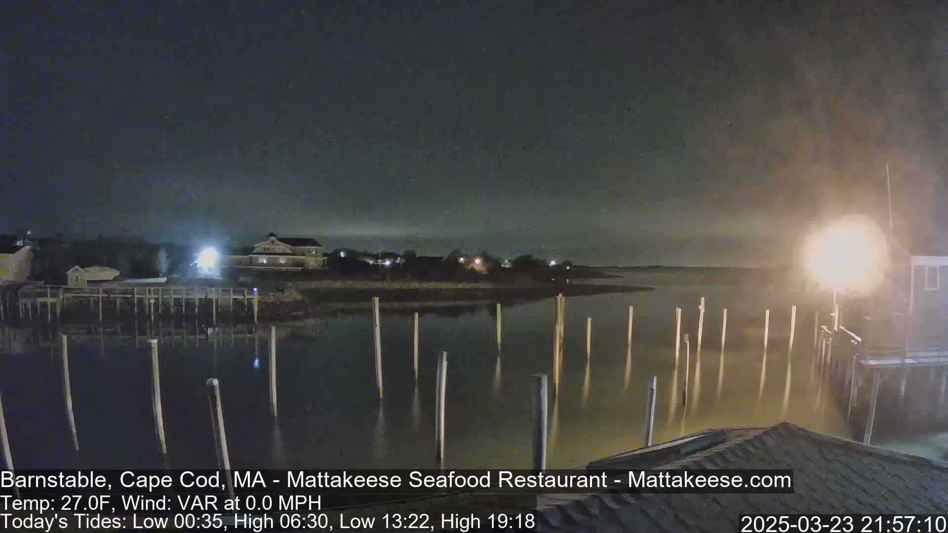 A nighttime view of a calm harbor with numerous pilings extending into the water, under a dark, slightly hazy sky.