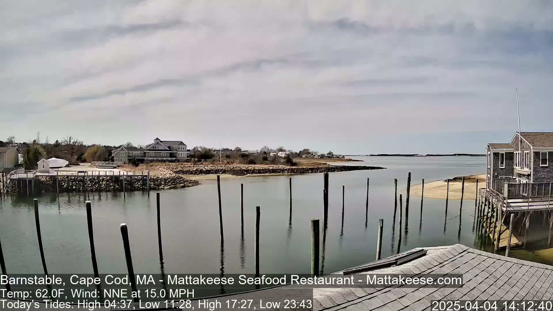 A calm body of water with numerous pilings, houses on a shoreline, and an overcast sky.
