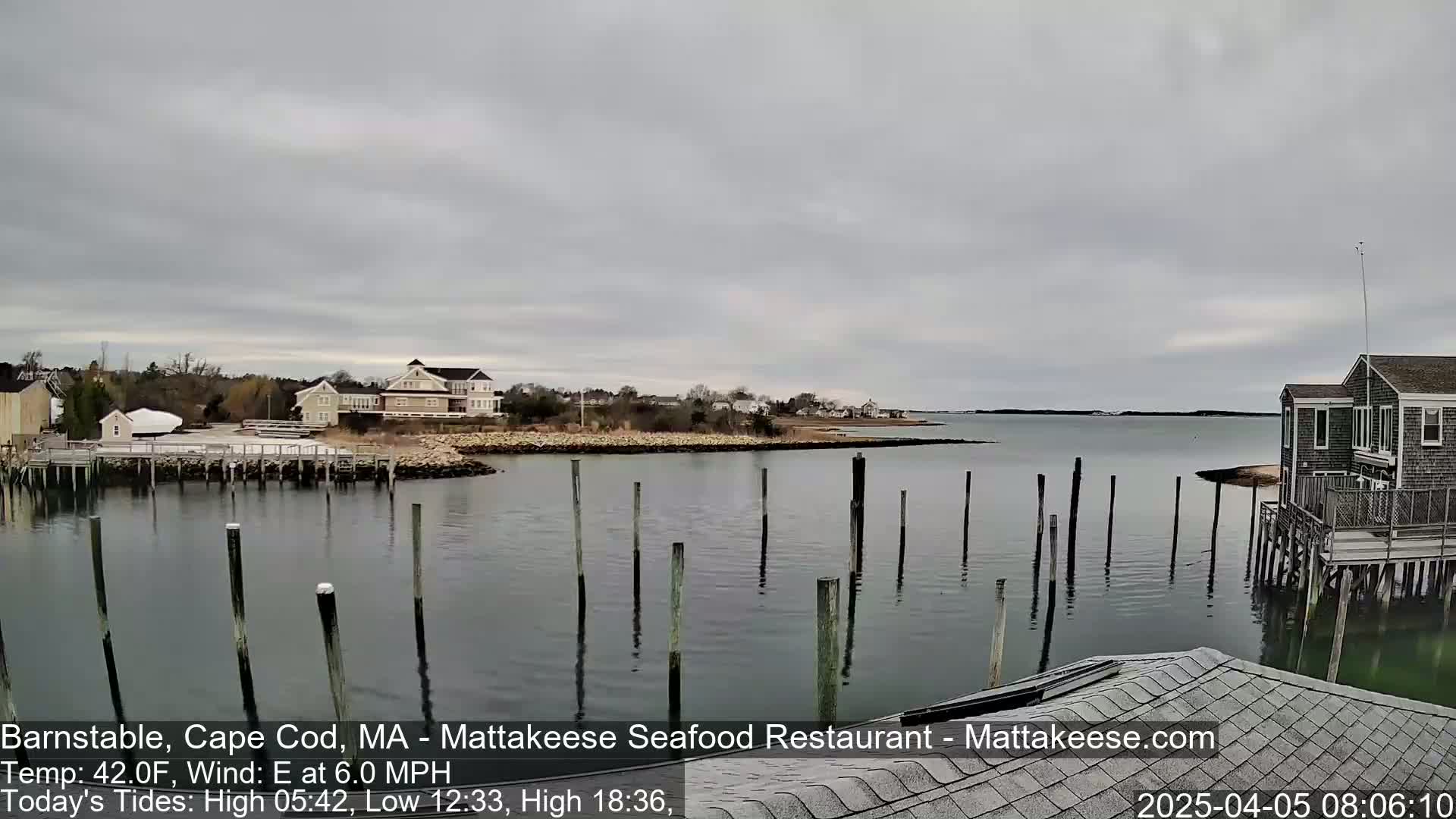 A calm body of water with numerous pilings and a few buildings on the shoreline under an overcast sky.