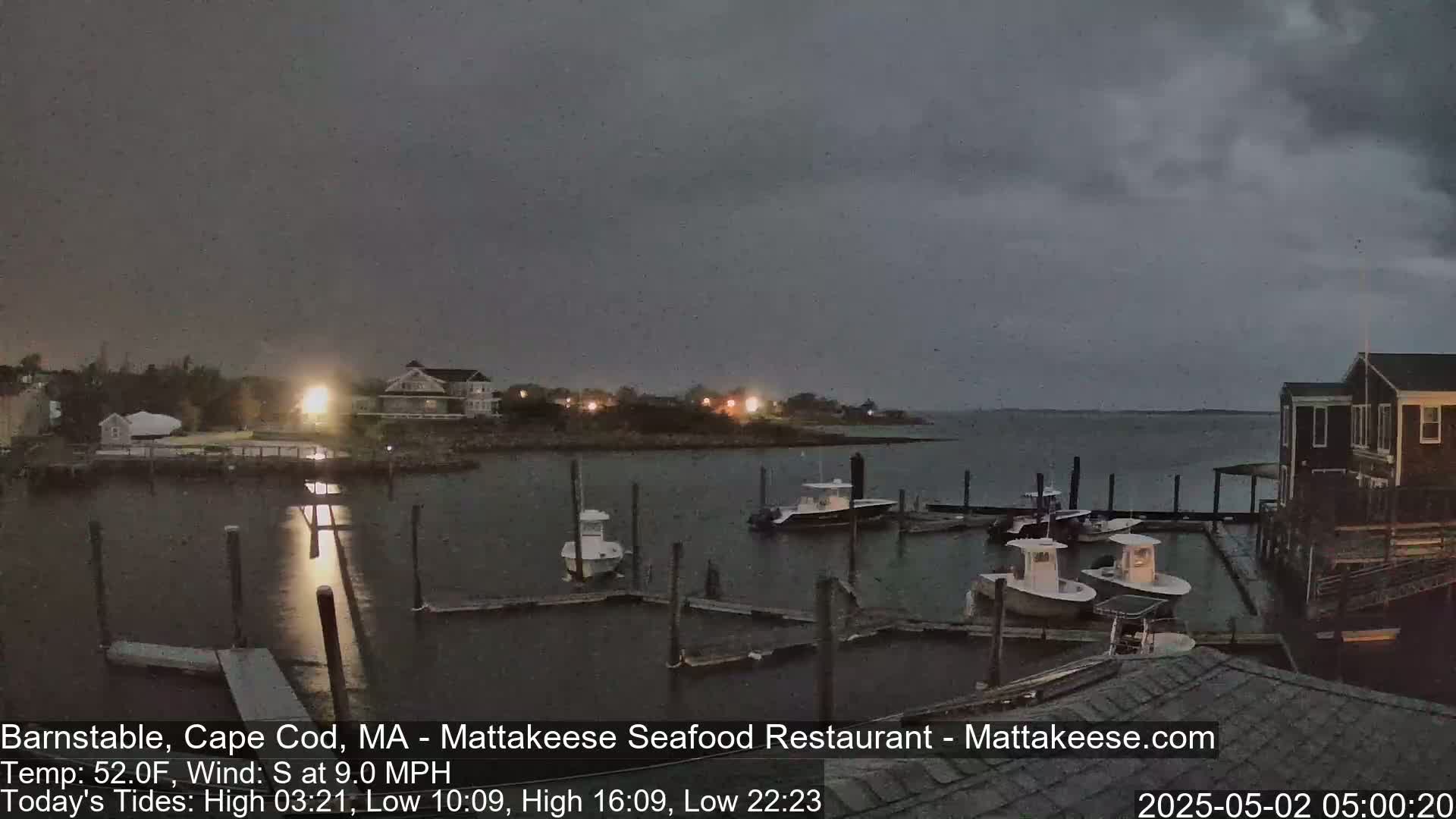 Several boats are moored at a dock under a dark, overcast sky.