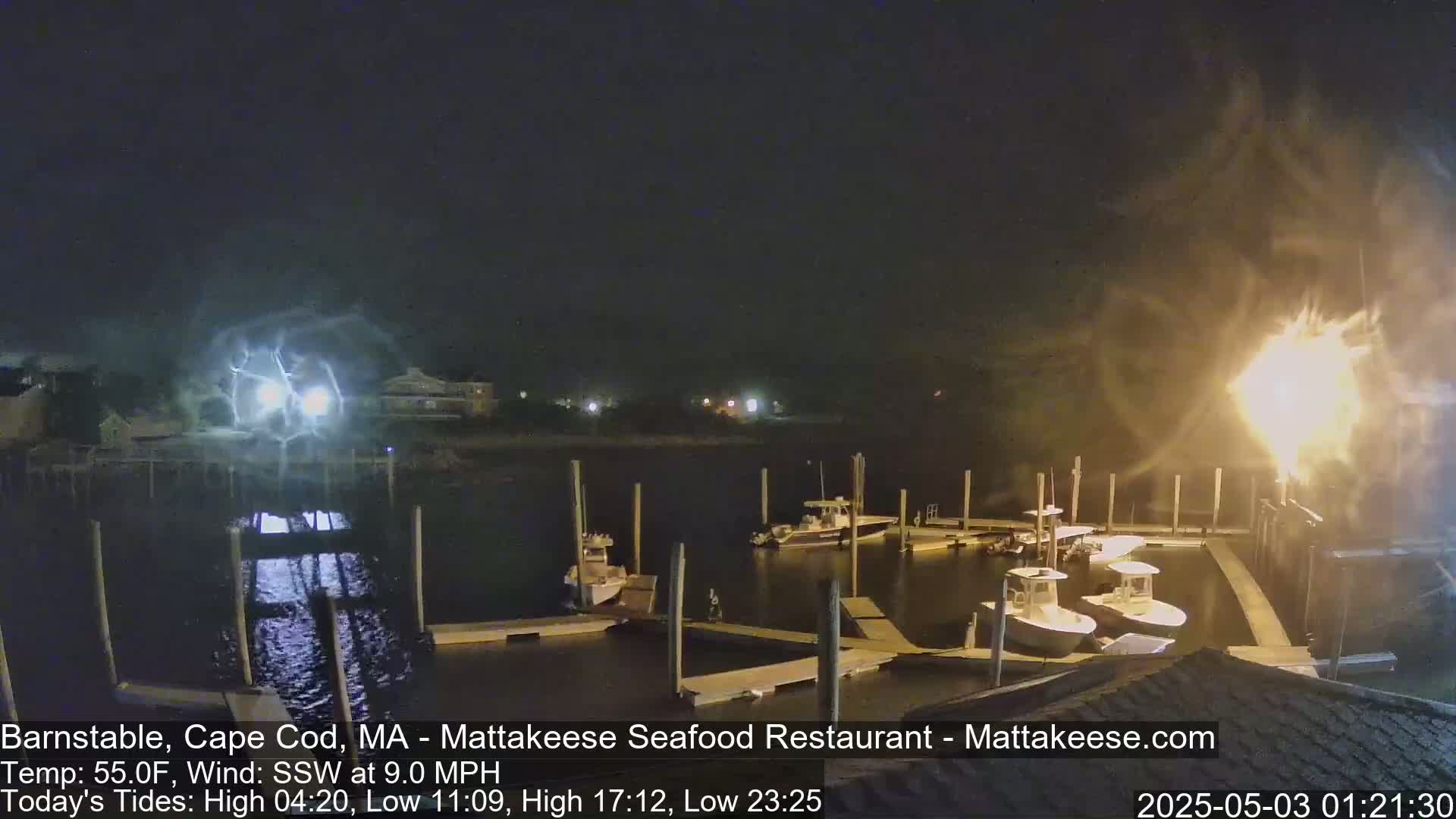 Several boats are docked at a marina at night under a dark, stormy sky with lightning visible in the distance.