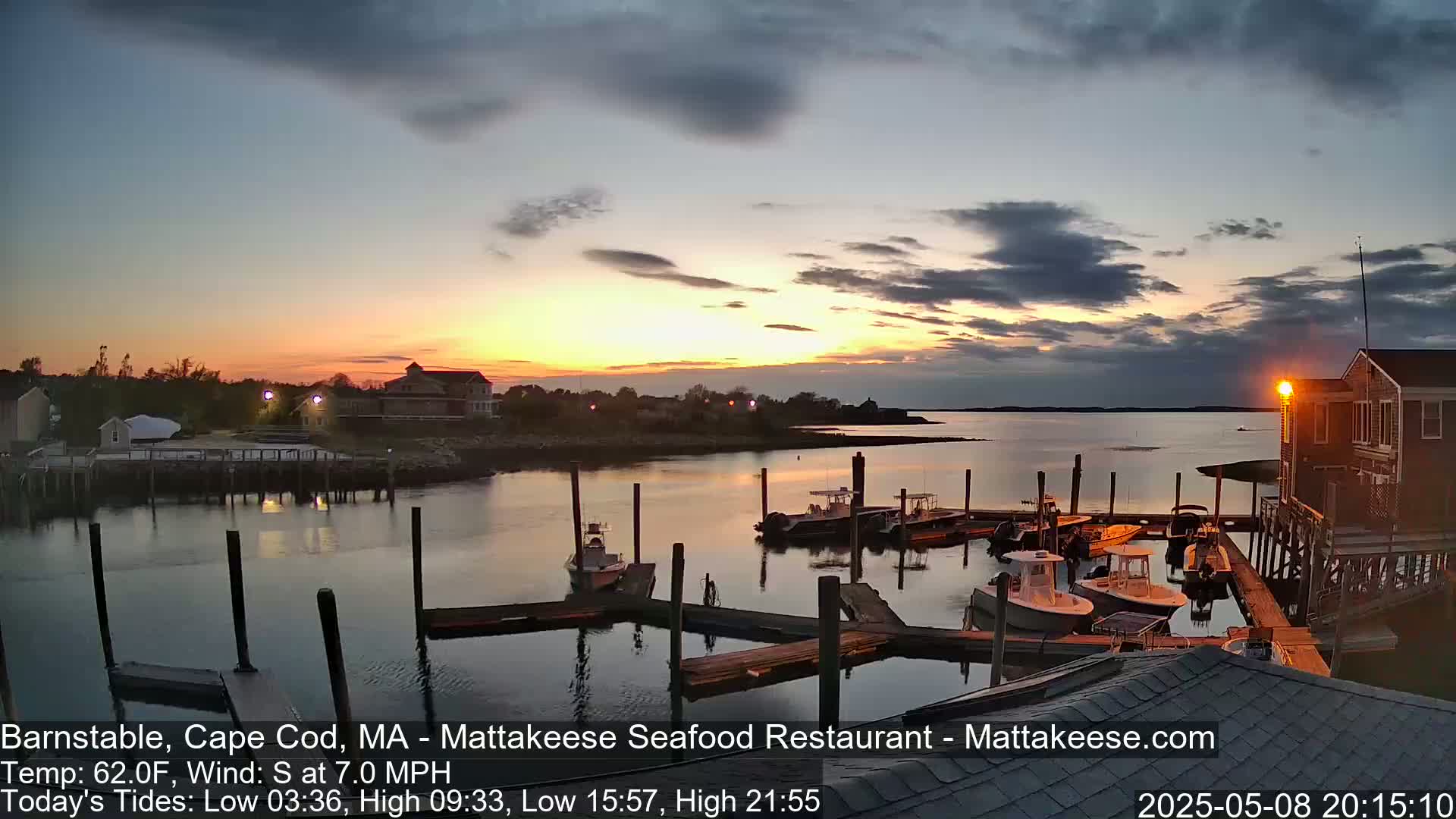 A sunset over a calm harbor with several boats docked at piers, under a partly cloudy sky.