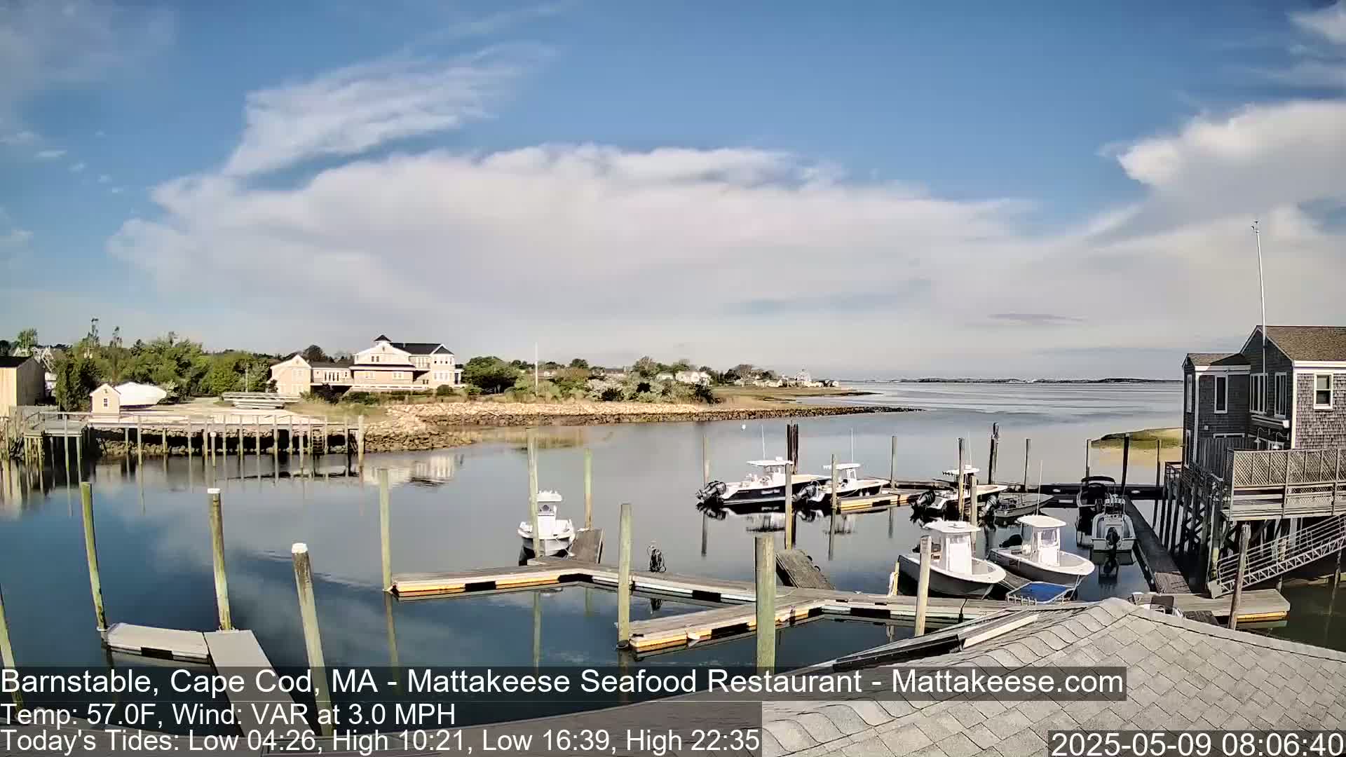 Several boats are moored at a marina on a calm, partly cloudy day.
