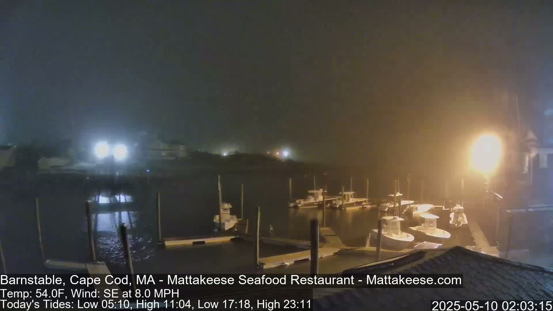 A nighttime harbor scene shows several boats moored at docks under hazy, foggy conditions with a southeast wind.