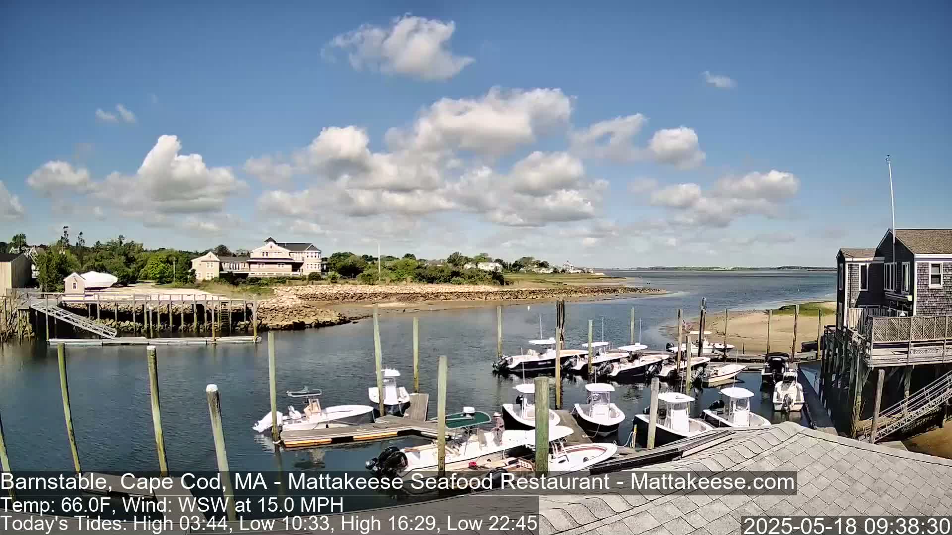 A partly cloudy day shows a harbor with numerous small motorboats docked near buildings, under a mostly sunny sky with some fluffy clouds.