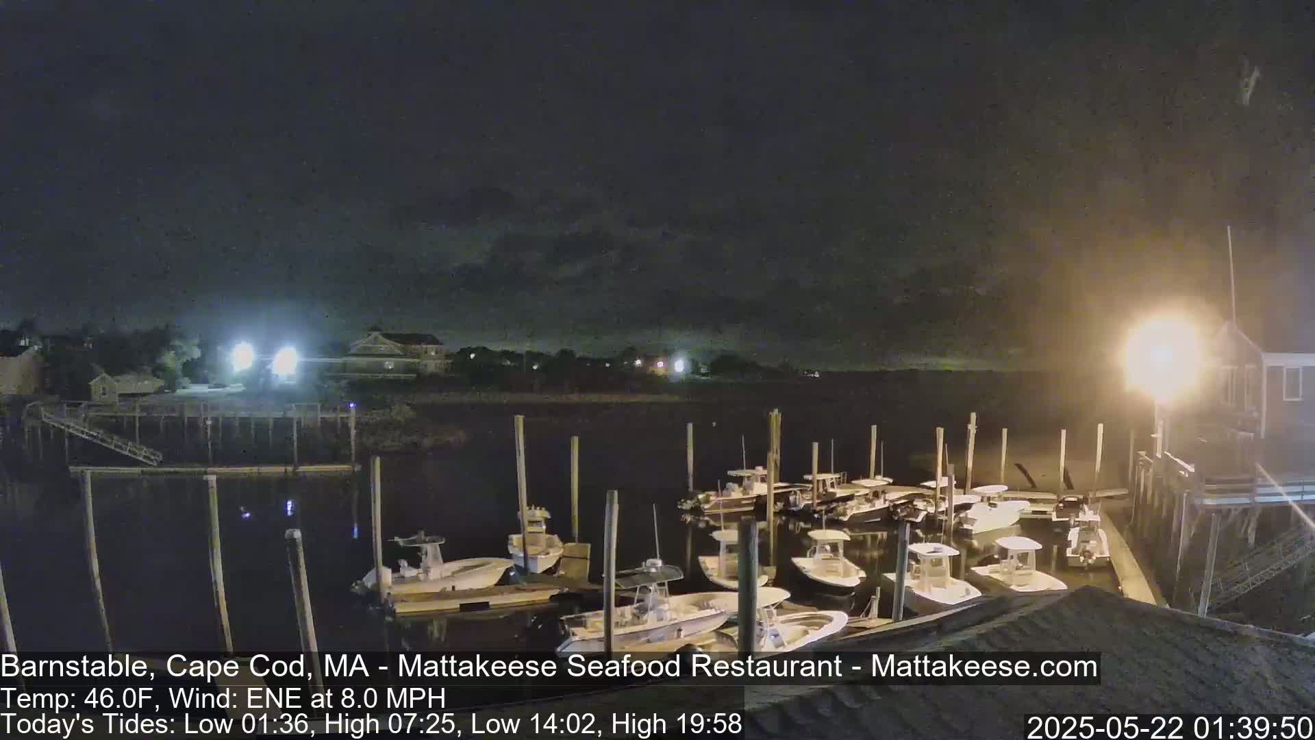A nighttime view of several boats moored at a dock under a partly cloudy sky.