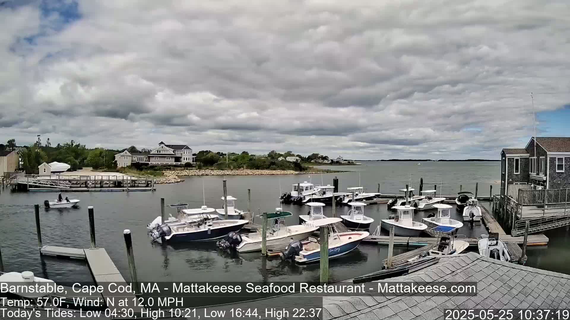 A partly cloudy day shows many small motorboats docked at a marina, with calm water and buildings visible in the background.