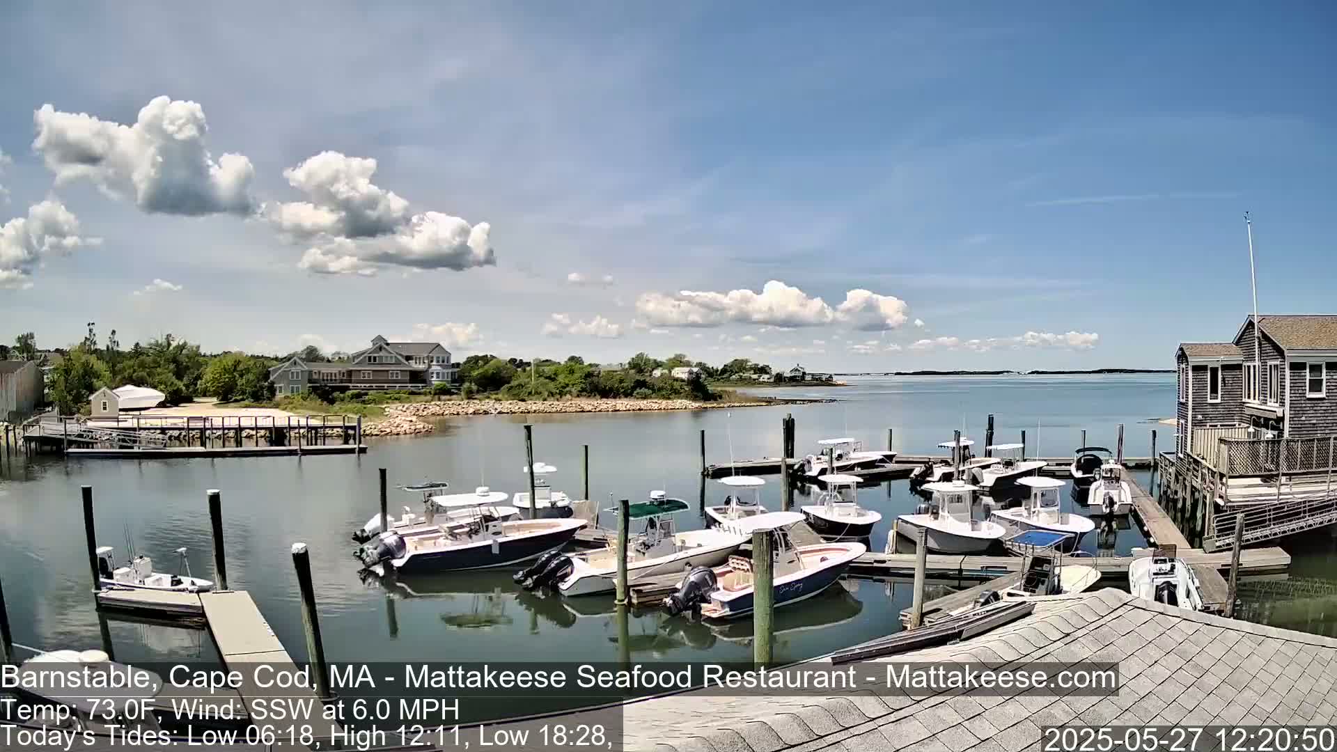 A sunny day with partly cloudy skies shows a harbor filled with numerous docked motorboats, some houses and buildings along the shoreline.