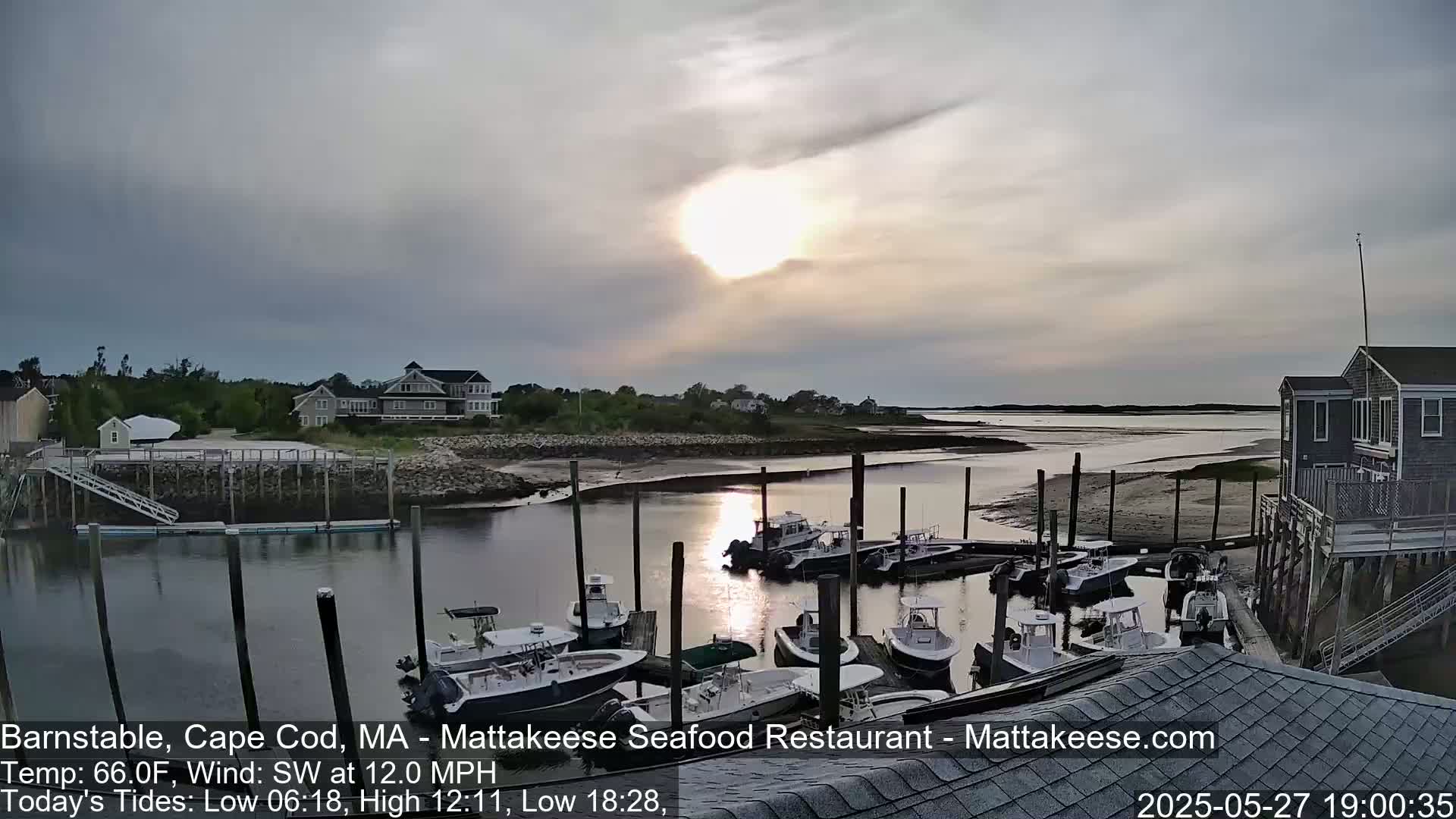 A mostly cloudy sunset over a calm harbor filled with docked boats and houses along the shore.