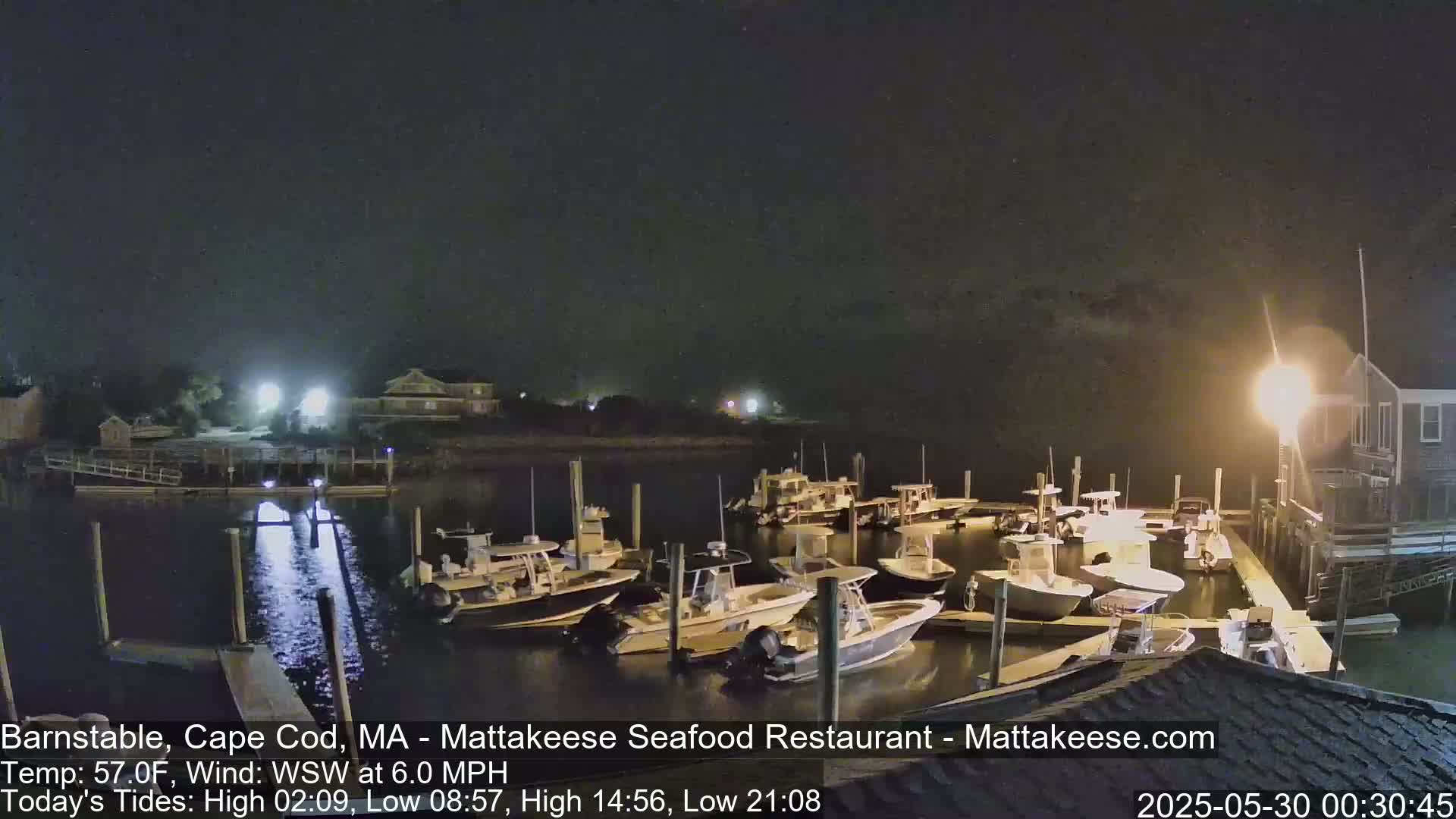 A nighttime view of a marina with numerous boats docked, under a dark sky with a gentle wind.