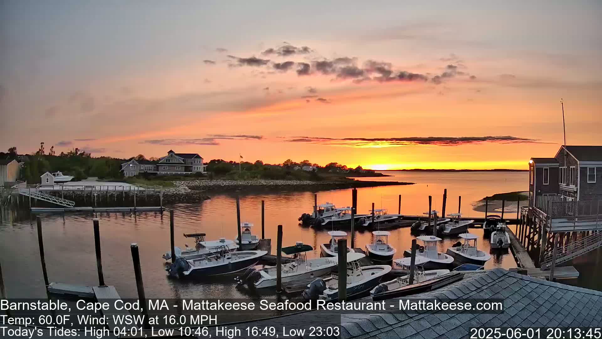 A harbor filled with docked motorboats at sunset under a mostly clear, orange-hued sky.