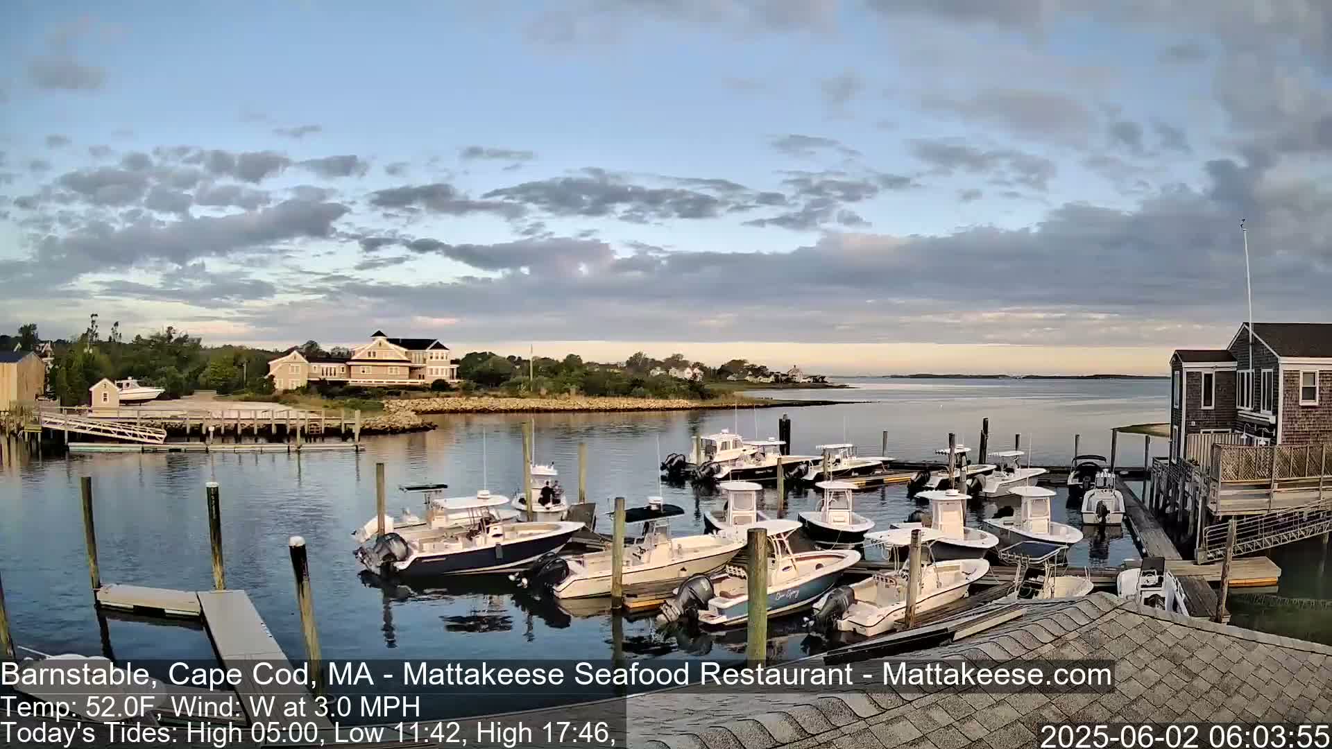 Many motorboats are docked at a calm harbor under a partly cloudy sky.